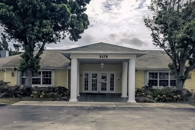 Senior living facility front entrance with columns, double doors, and landscaping.