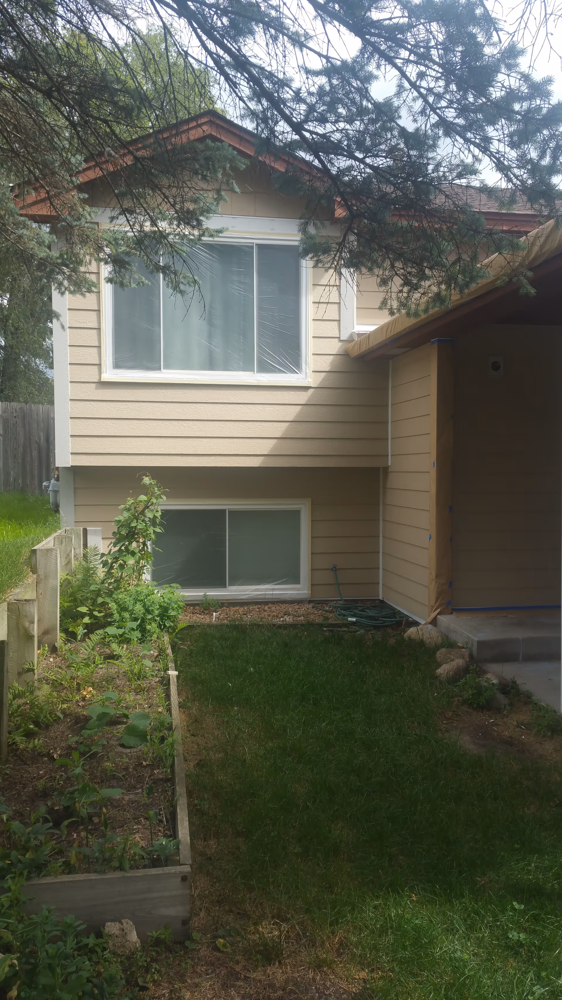Beige two-story house exterior with windows, a small garden, and front yard.