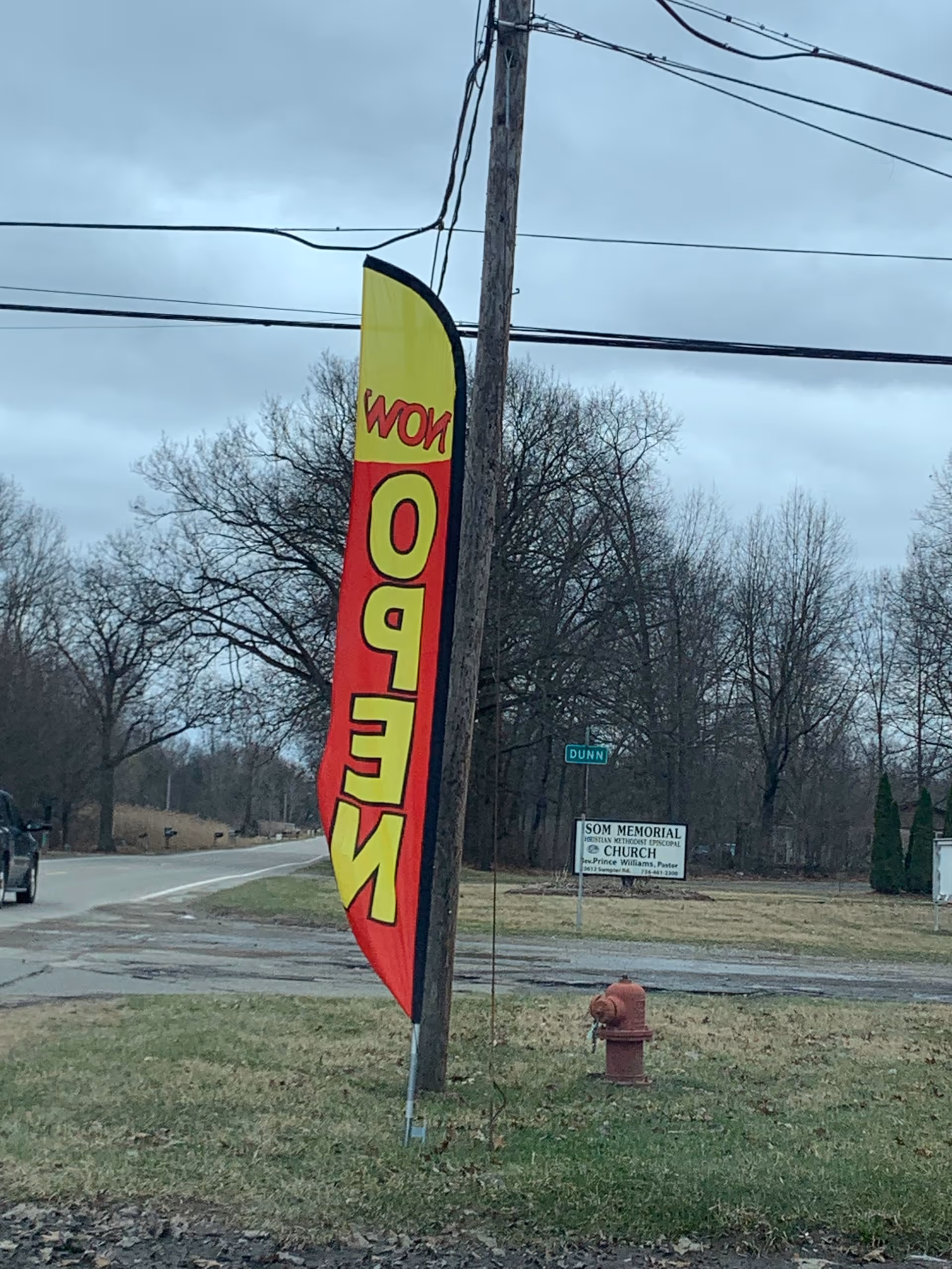 Tall yellow and red open banner beside a street with trees and a fire hydrant.