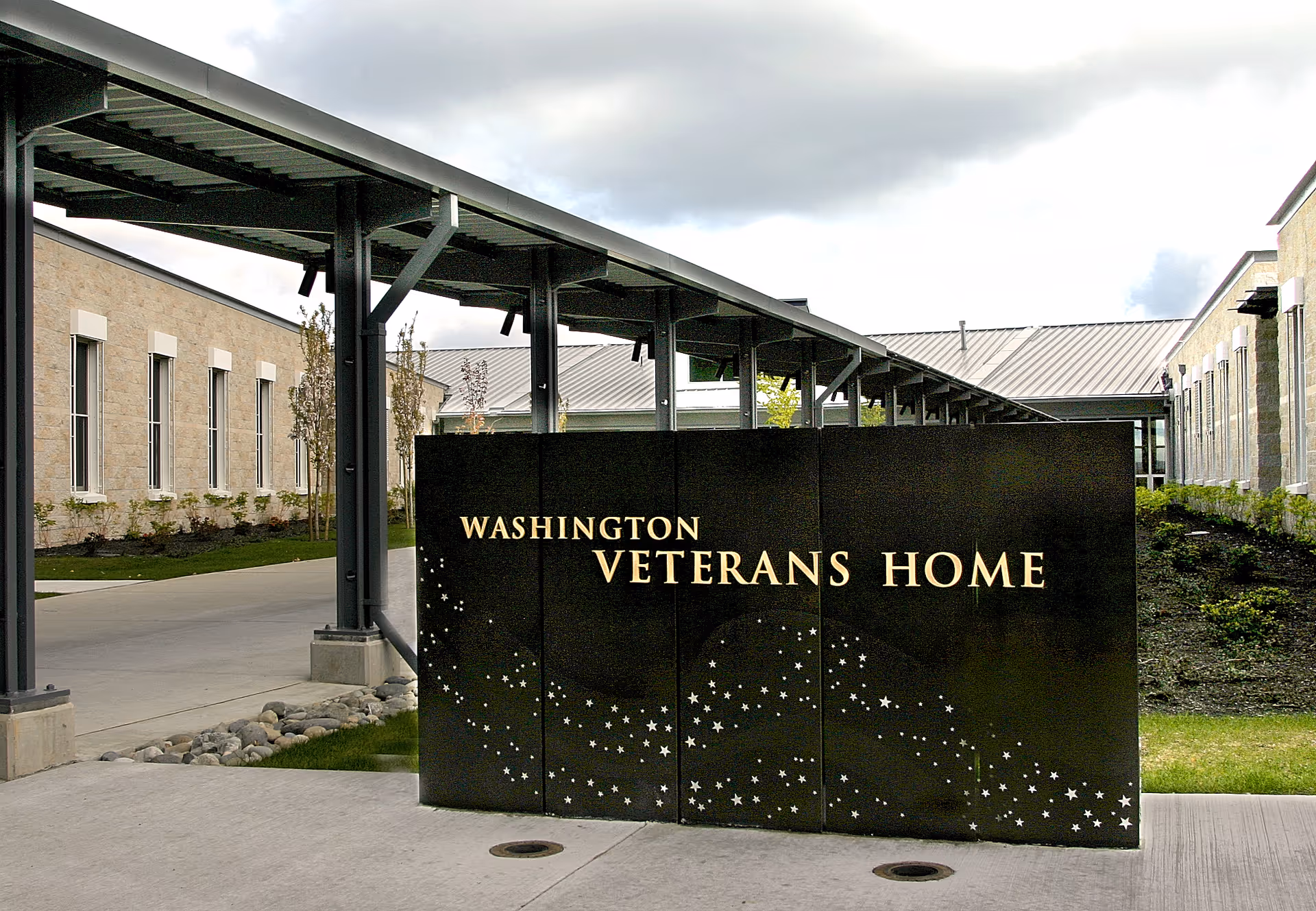 Entrance sign reading 'Washington Veterans Home' in front of a covered walkway and low stone buildings.