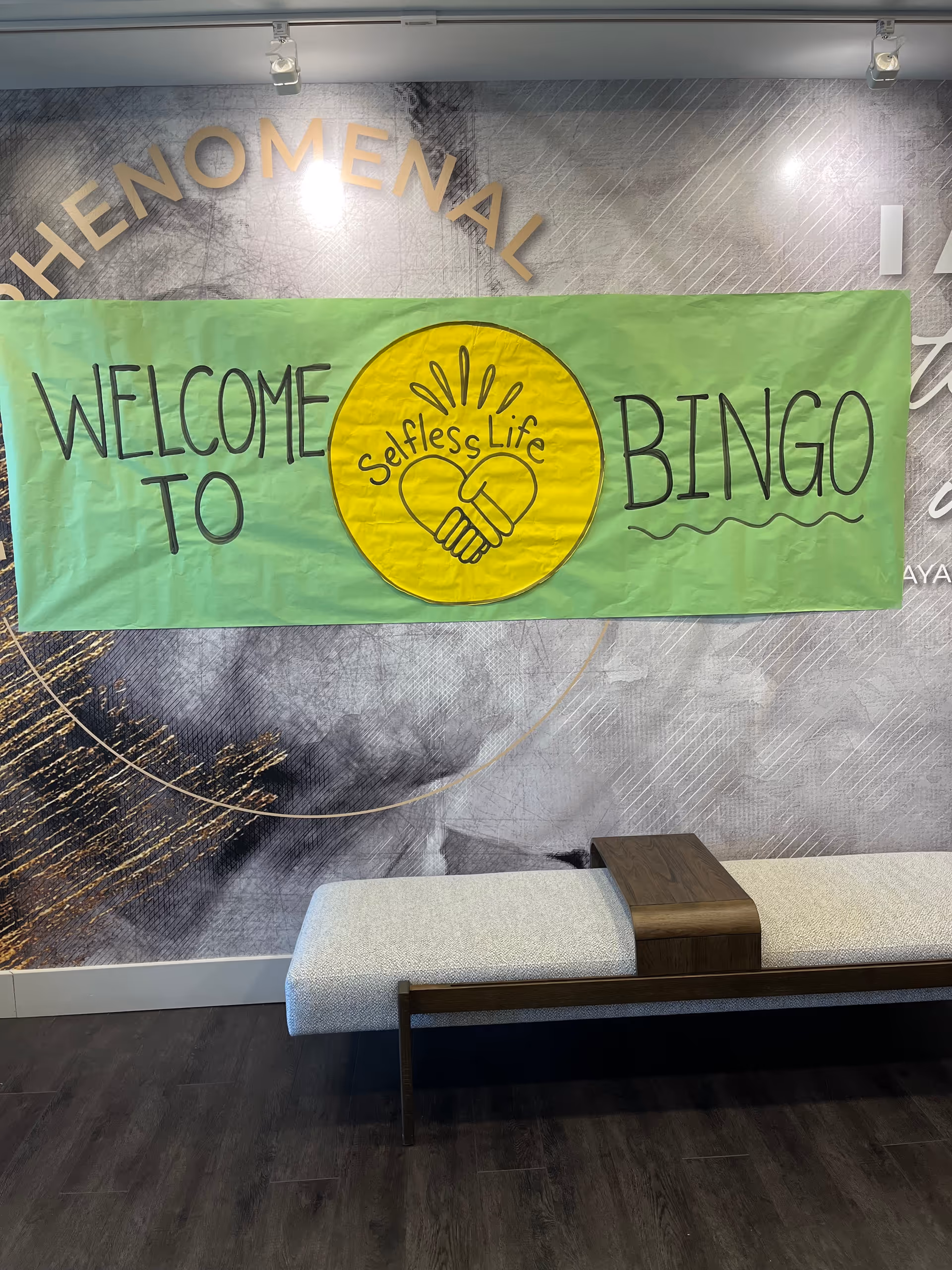 Green banner reading Welcome to Bingo with Selfless Life logo hung on a wall.
