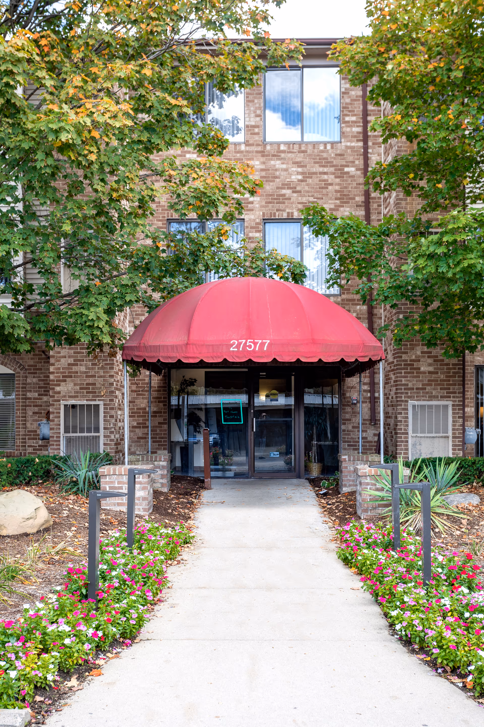Brick senior living building with red canopy entrance and landscaped walkway.