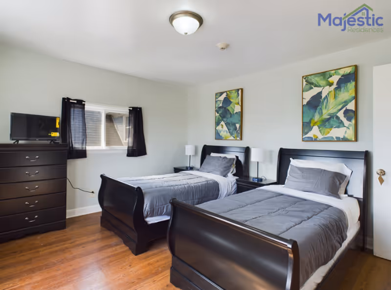 Two twin beds in a bright shared room with dark wood furniture, a dresser, and TV.