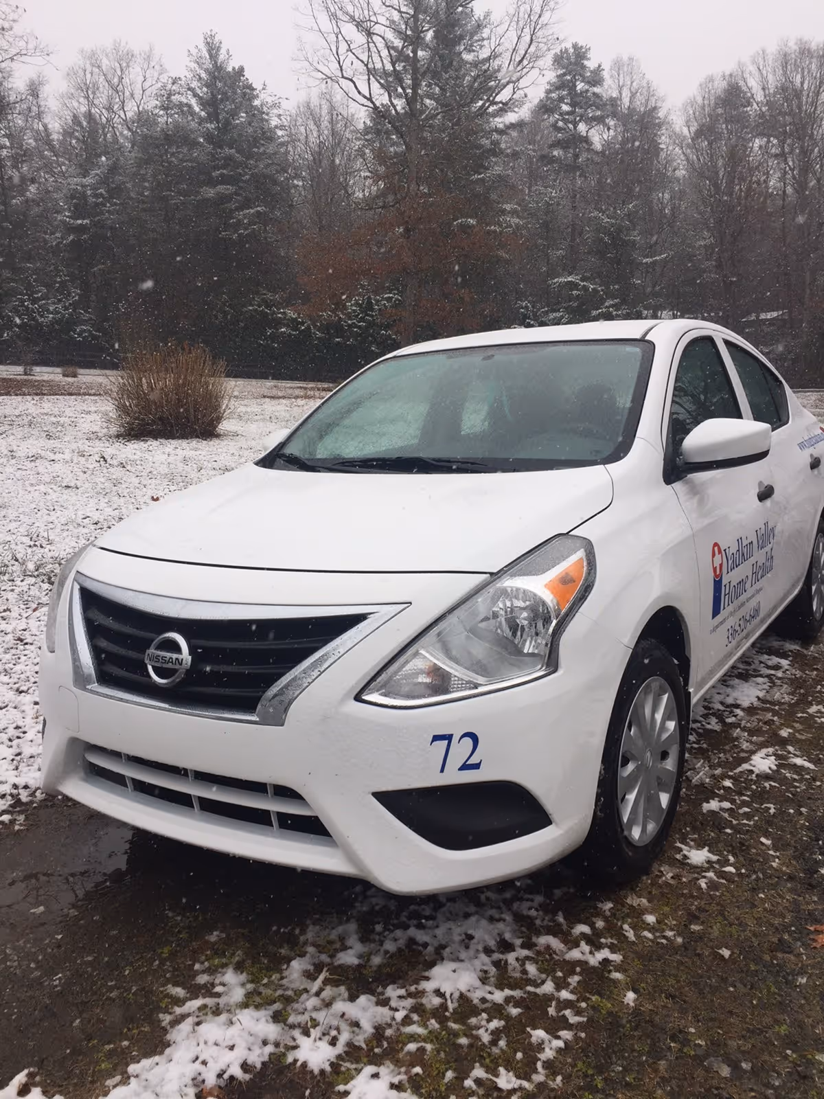 White Nissan sedan with blue 72 and Home Health logo in snowy lot.