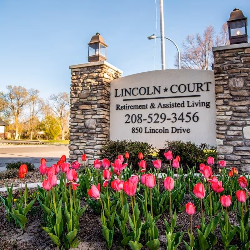 Stone entrance sign reading 'Lincoln Court Retirement & Assisted Living' with pink tulips in the foreground.