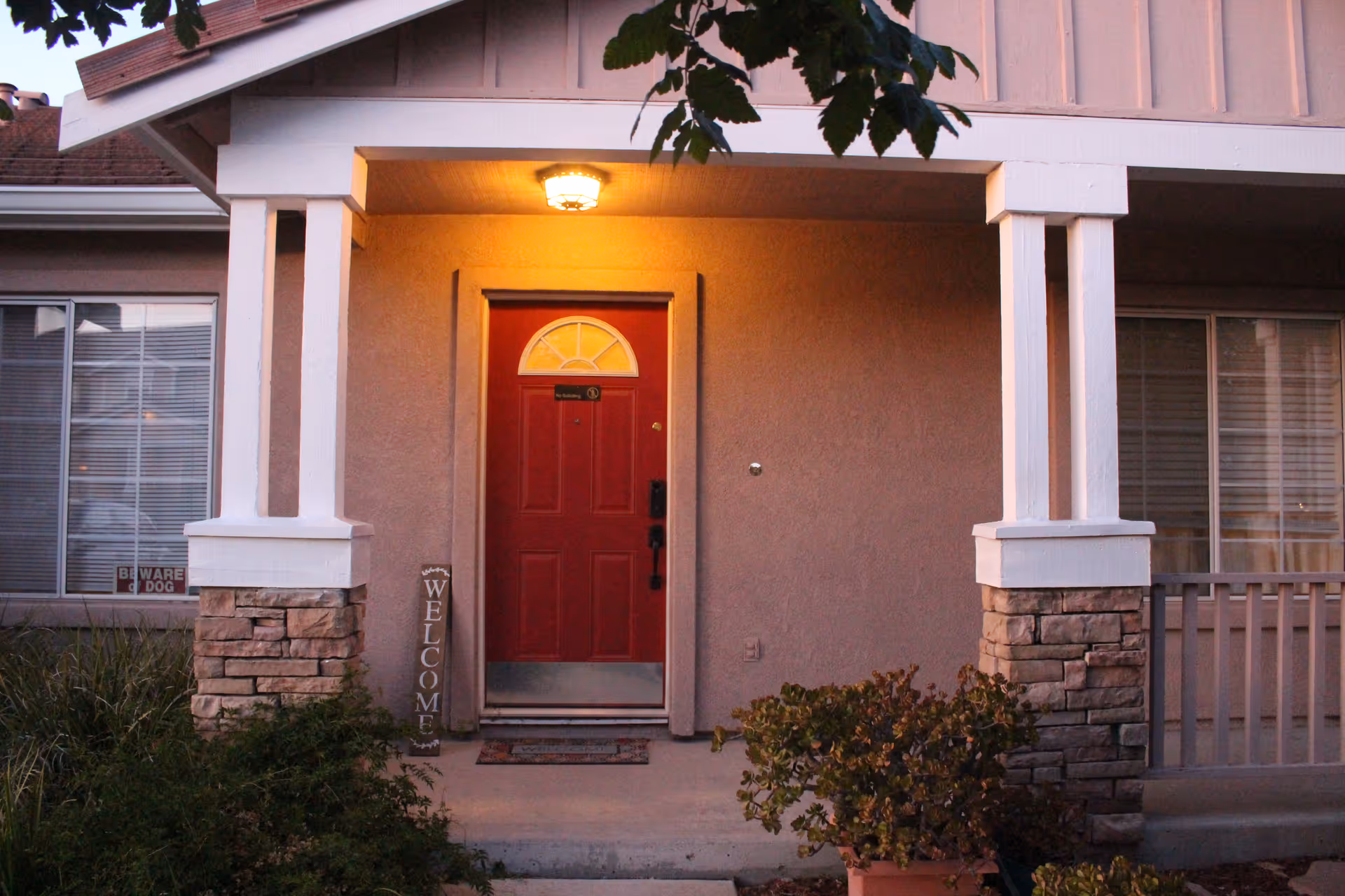 Residential-style building entrance with red front door, porch columns, and a welcome sign.