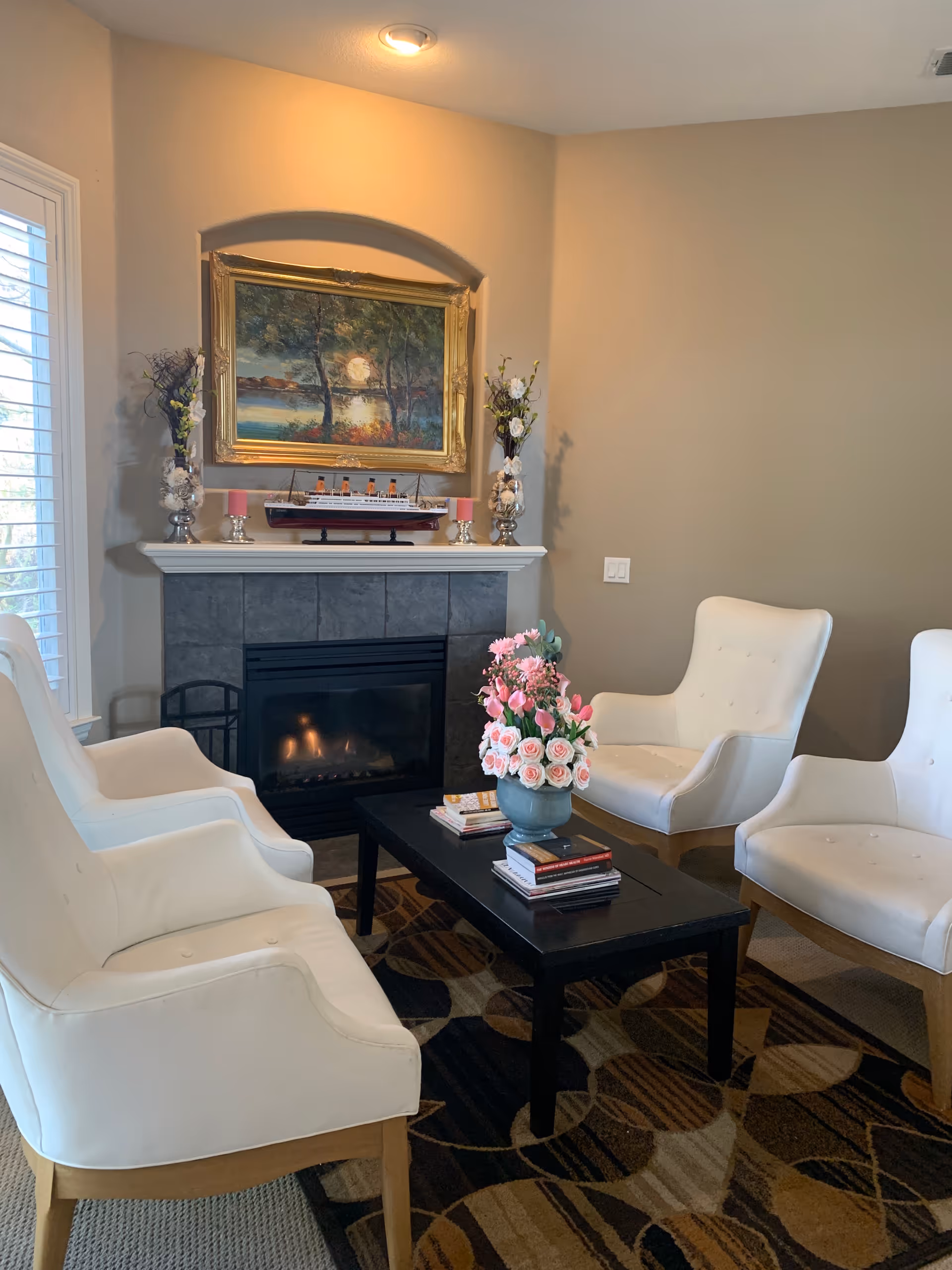 Cozy living room with four white chairs around a coffee table in front of a fireplace.