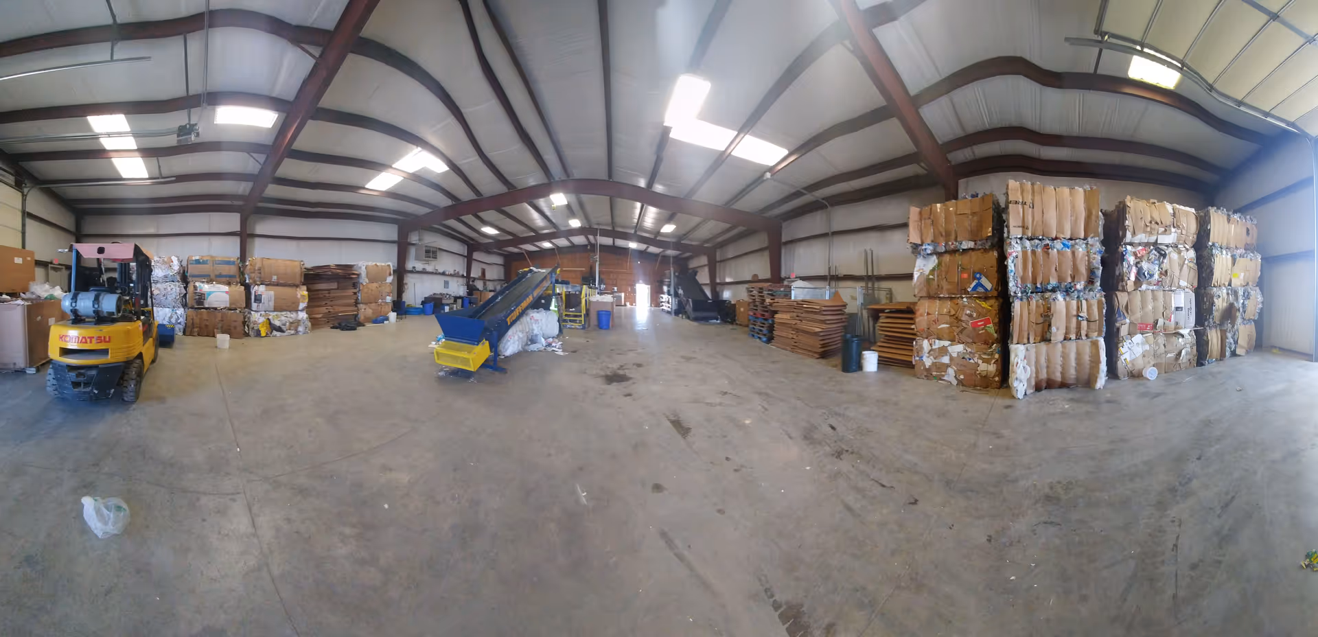 Inside a large warehouse with stacked cardboard bales and a forklift.