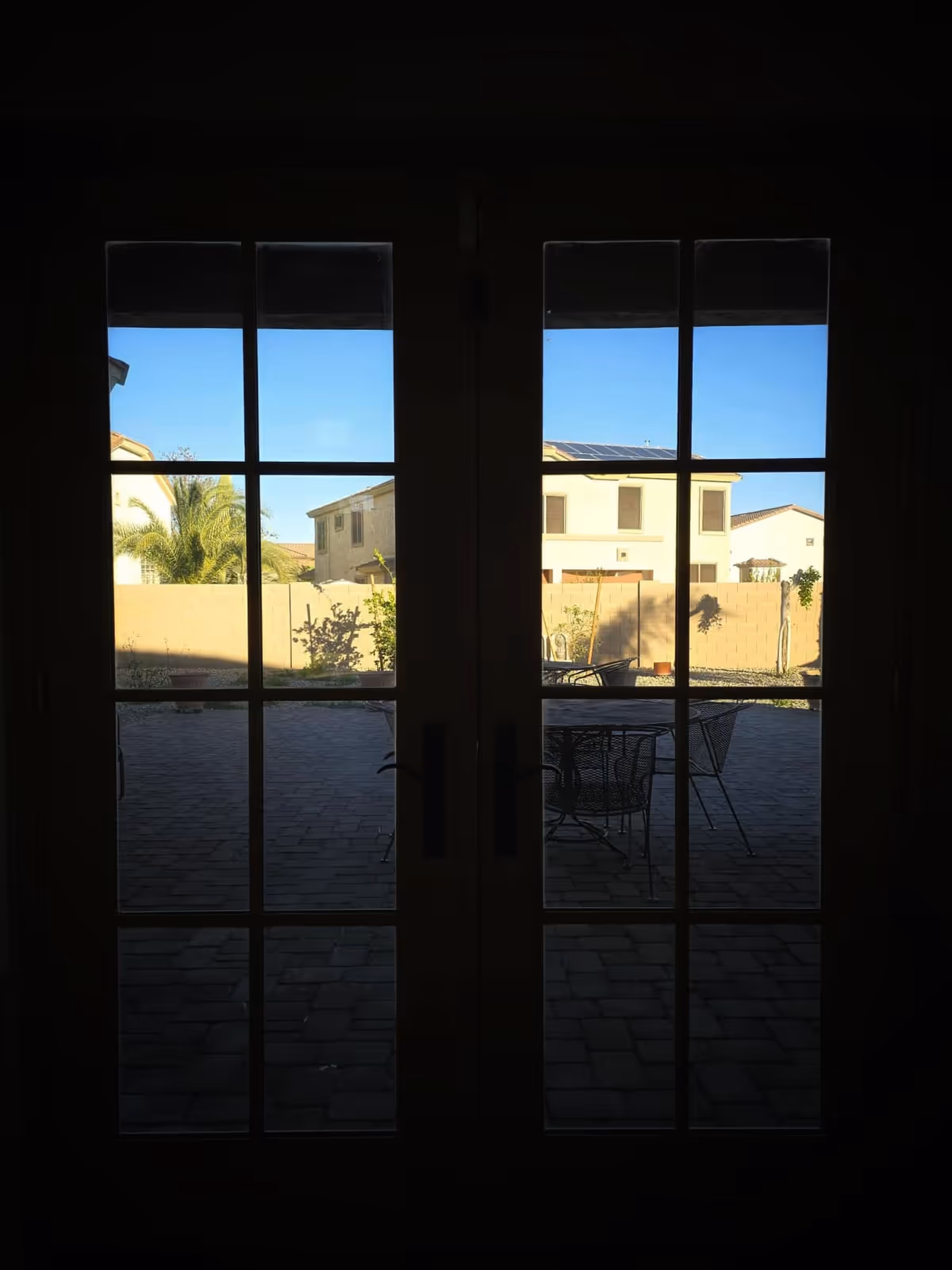 Dark interior view through French doors opens to outdoor patio with chairs.
