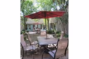 Outdoor patio with table, chairs, and a red umbrella in a sunny courtyard.
