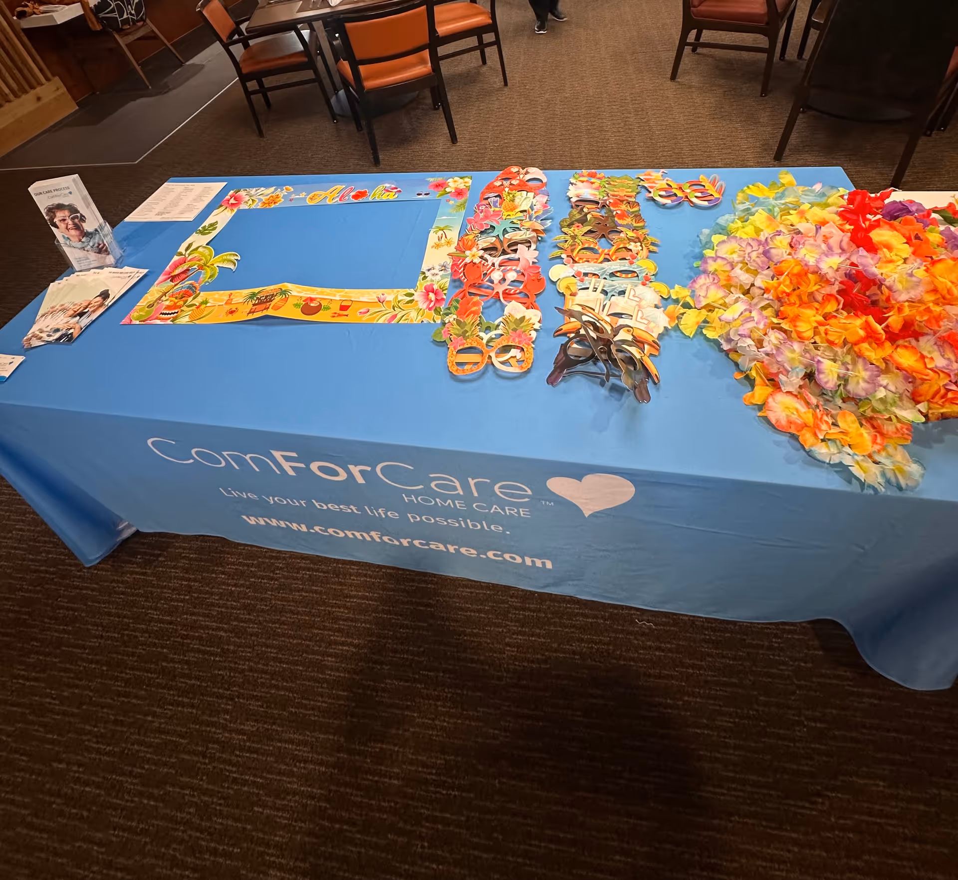 Blue-covered table displays leis, masks, and promotional materials for ComForCare inside.