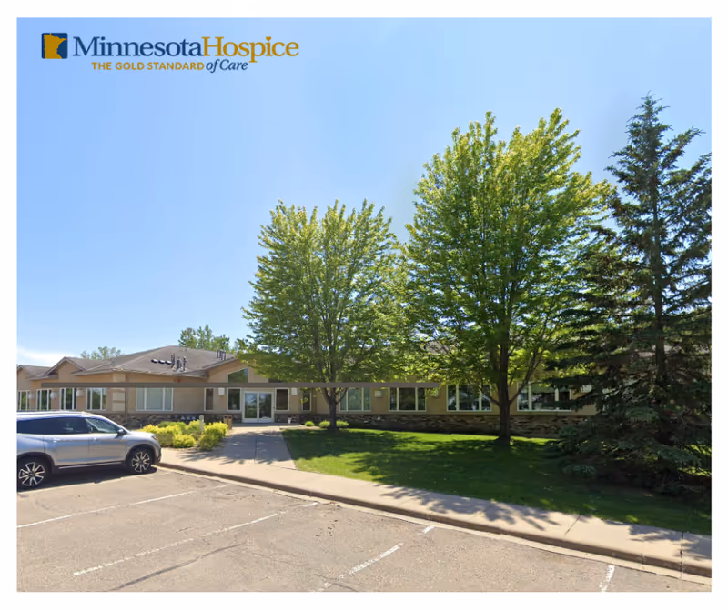 Exterior view of Minnesota Hospice building with trees, lawn, and a parked car in foreground.