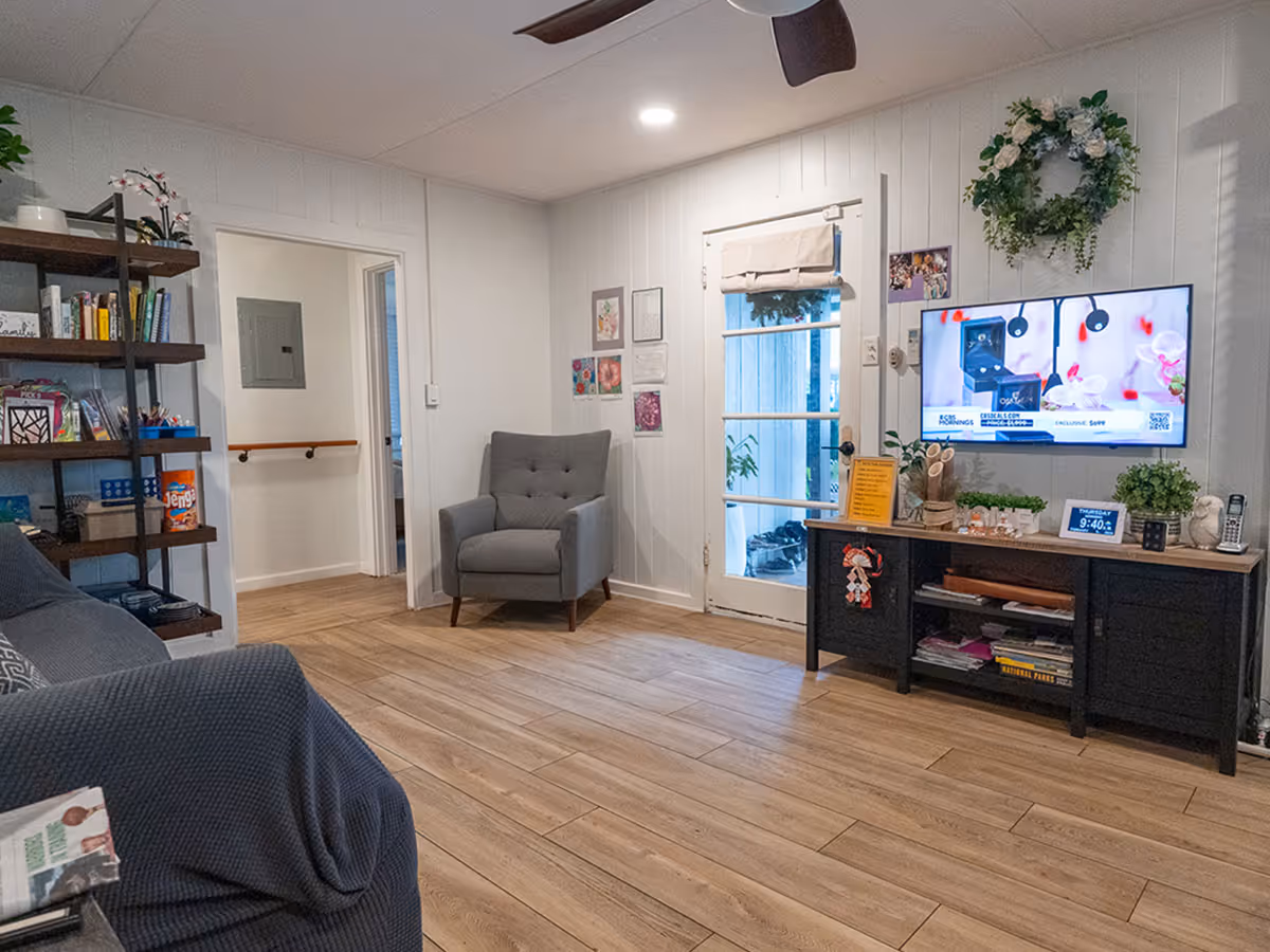 Cozy senior living room with a TV, sofa, armchair, and shelves.