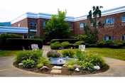 Brick senior living facility exterior with circular landscaped bed and fountain.