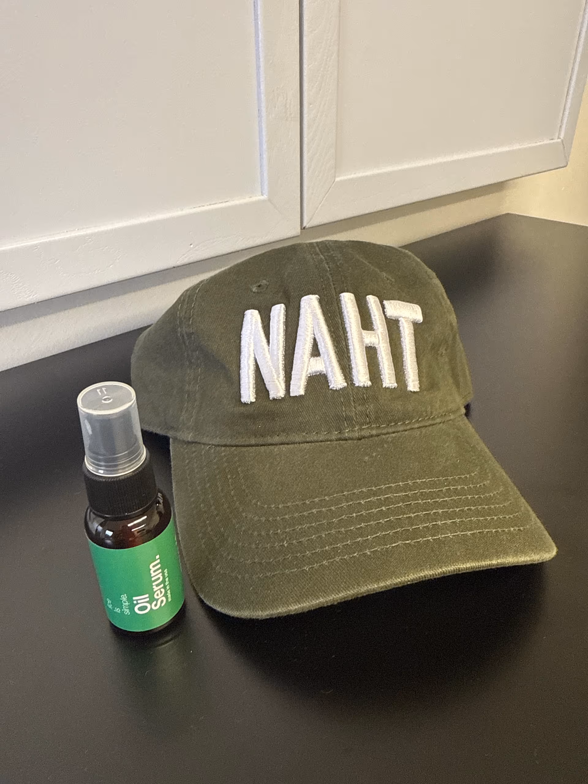 Close-up of a green NAHT hat and oil serum bottle on a dark kitchen counter.