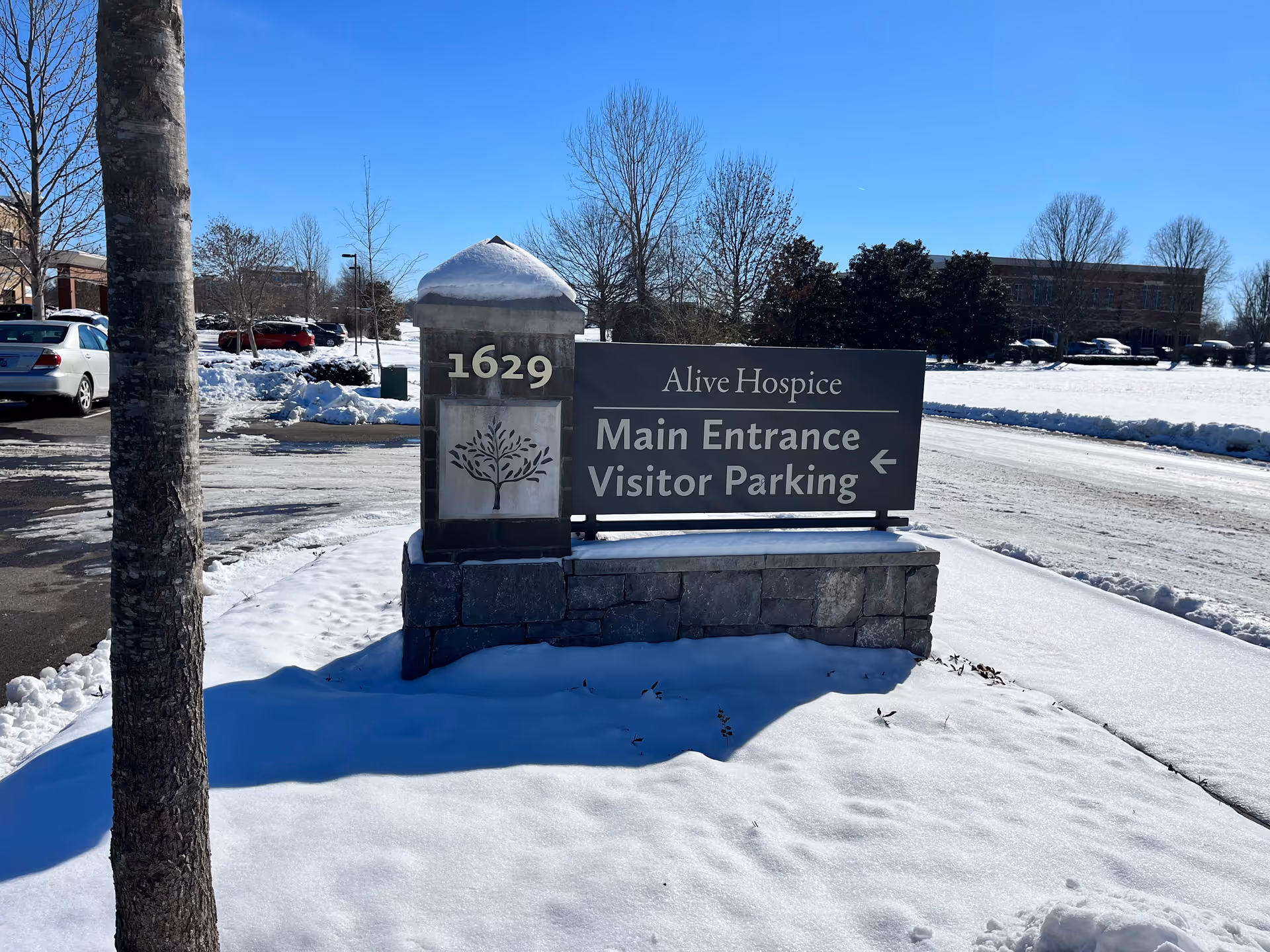 Snowy scene of Alive Hospice main entrance and visitor parking sign.