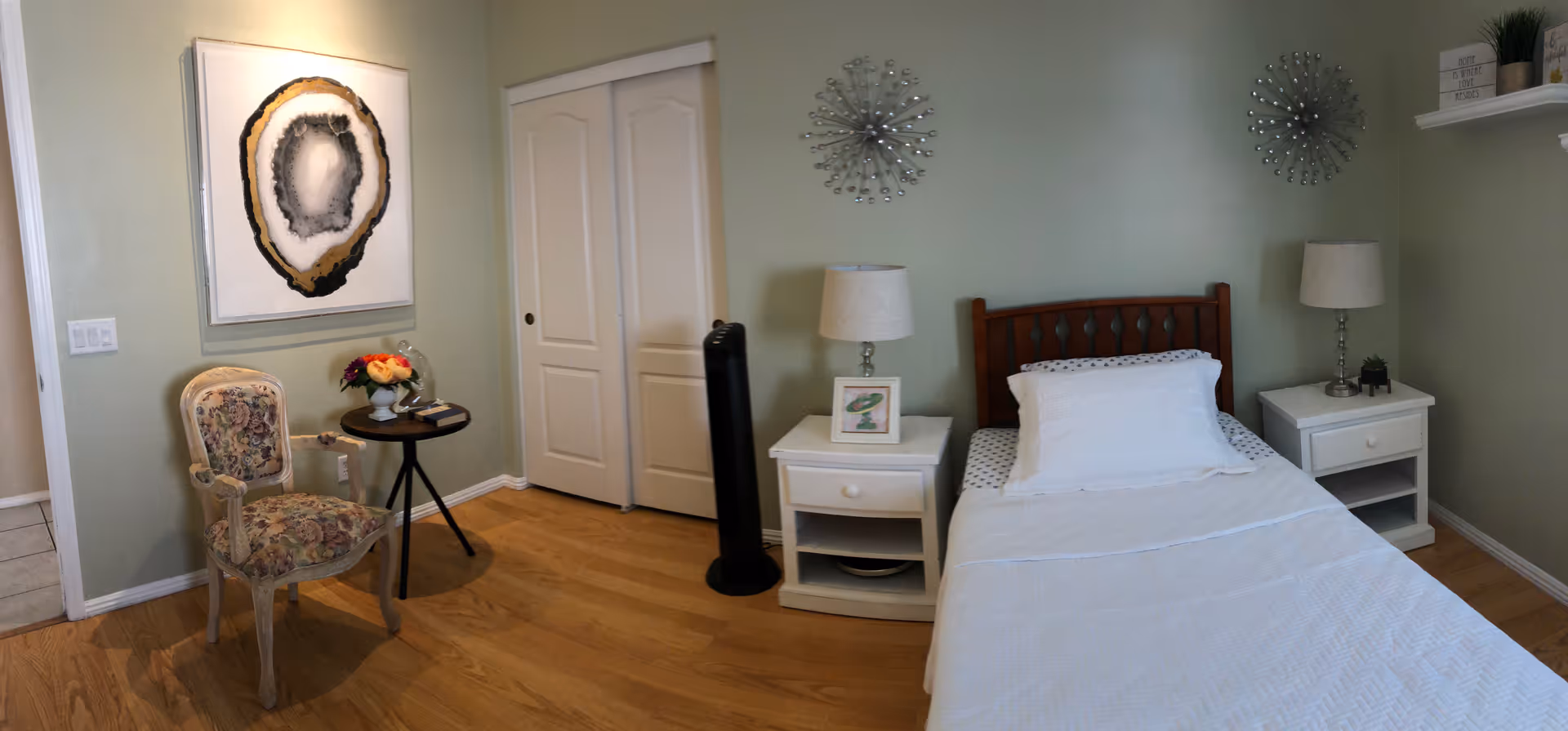 A well-lit senior living bedroom with a single bed, nightstands, lamps, and chairs.