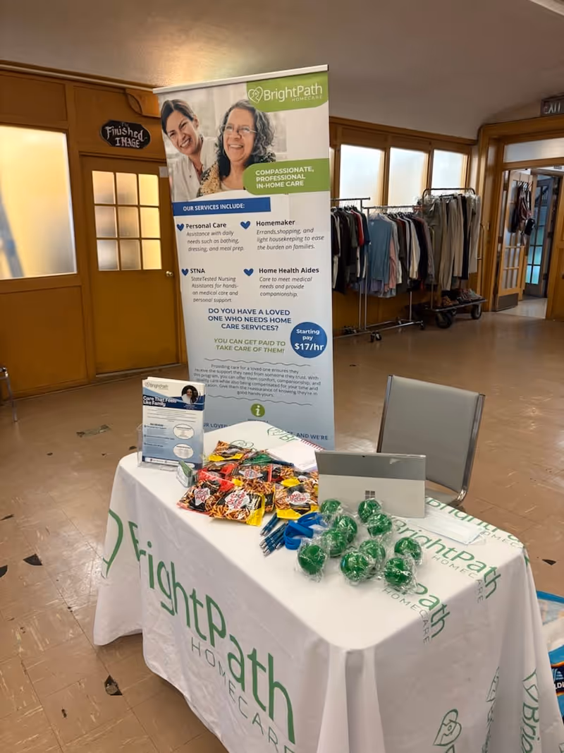 Indoor hallway features a BrightPath Home Care information booth with banner, table, and clothing rack.
