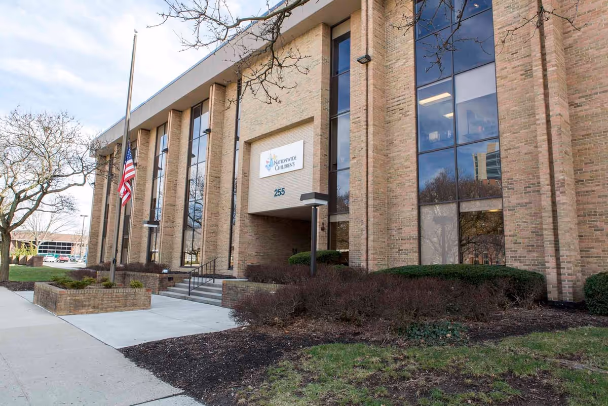 Brick building exterior with large windows, entrance, flagpole, and landscaping.