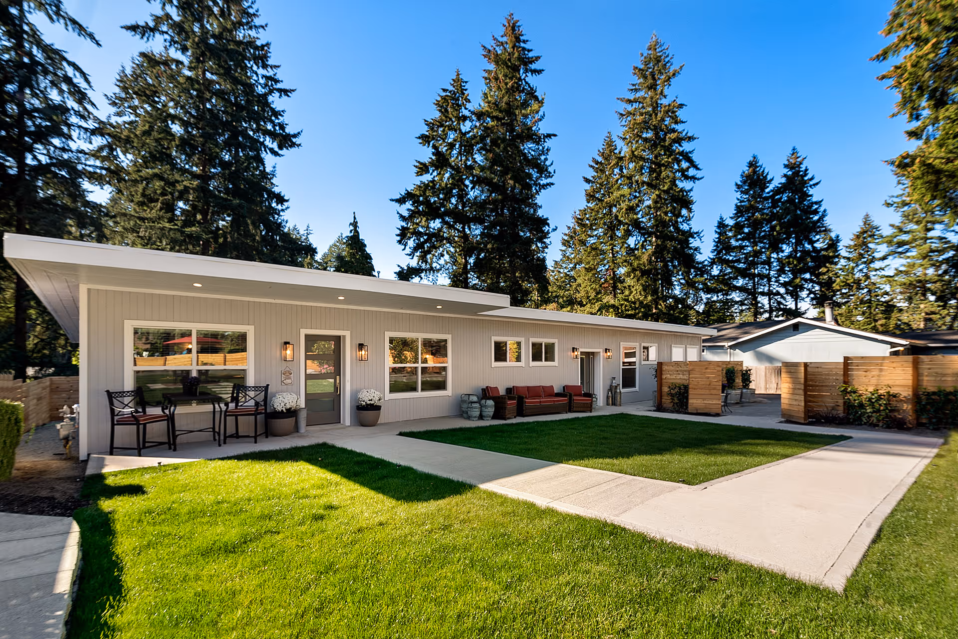 Single-story senior living building with a covered patio, outdoor seating, and a green lawn.