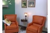 Two orange recliner chairs with a lamp and framed pictures in a small lounge.