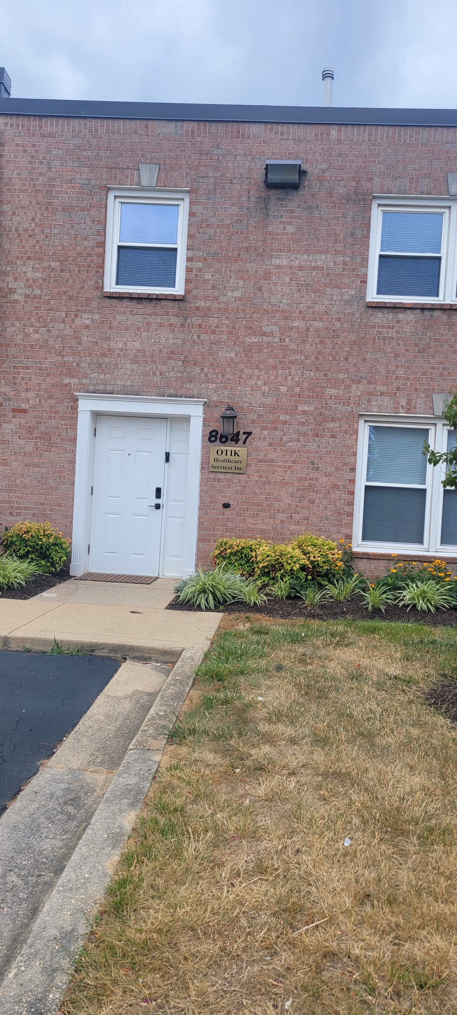 Brick senior living facility front shows OTIK Health Care Services sign beside a white entry door.