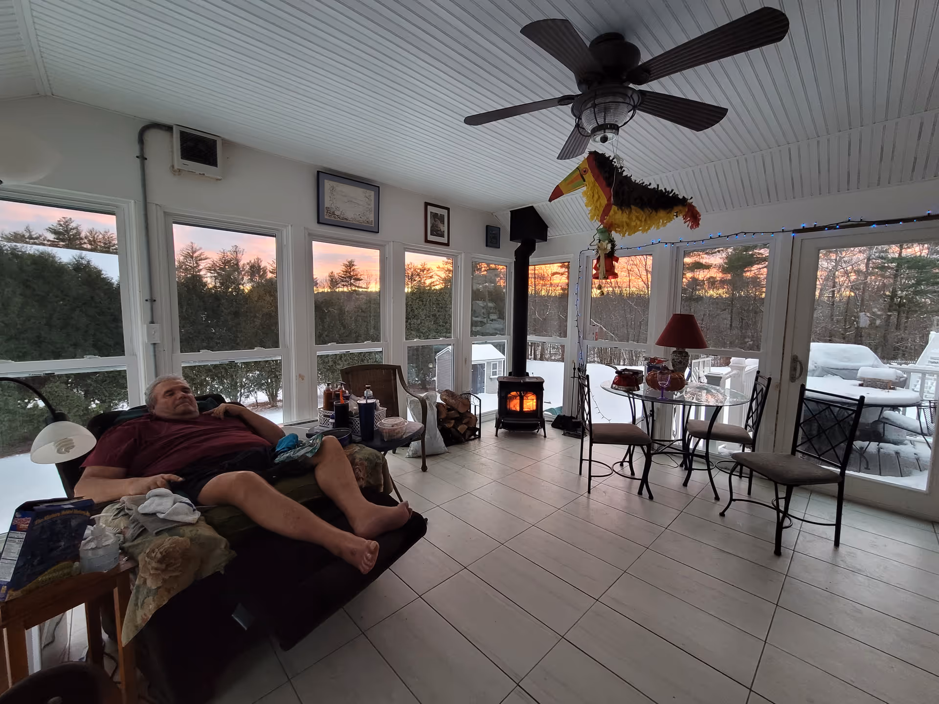 Resident lounging on a couch in a bright enclosed porch-style living room.