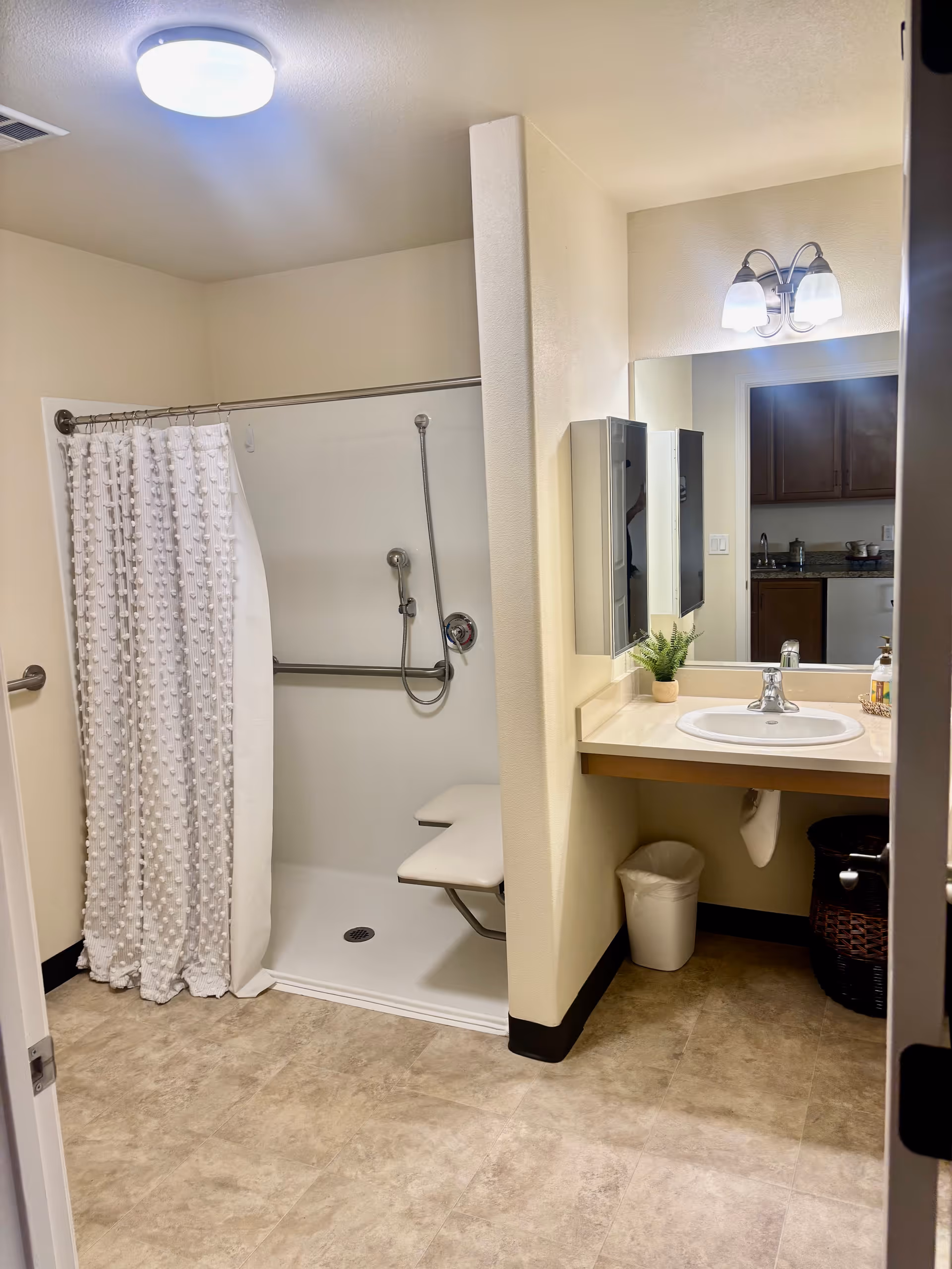 Senior living bathroom with a walk-in shower, shower chair, and sink with mirror.