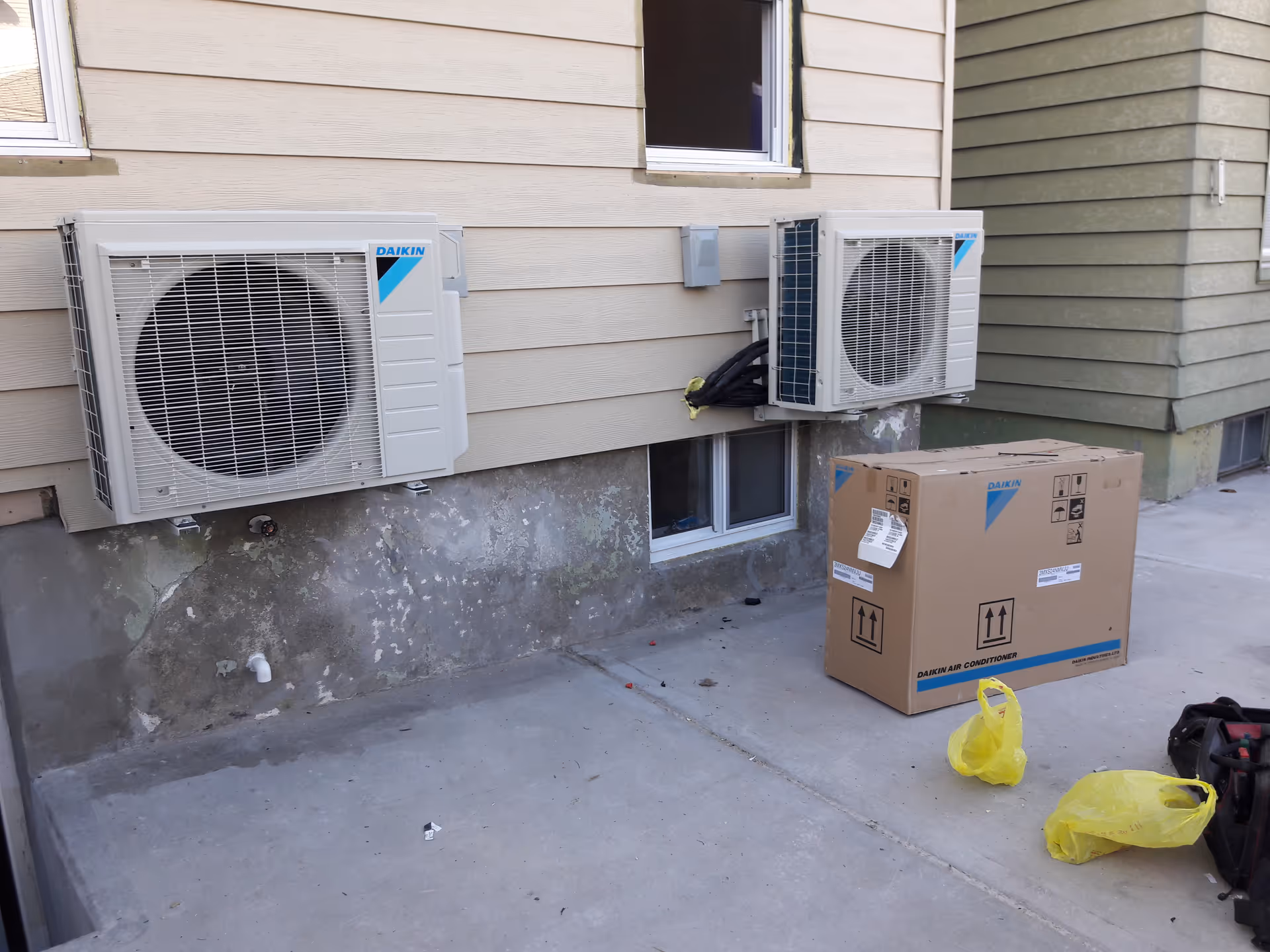 Exterior wall of a building with two Daikin air conditioner units and a cardboard box.