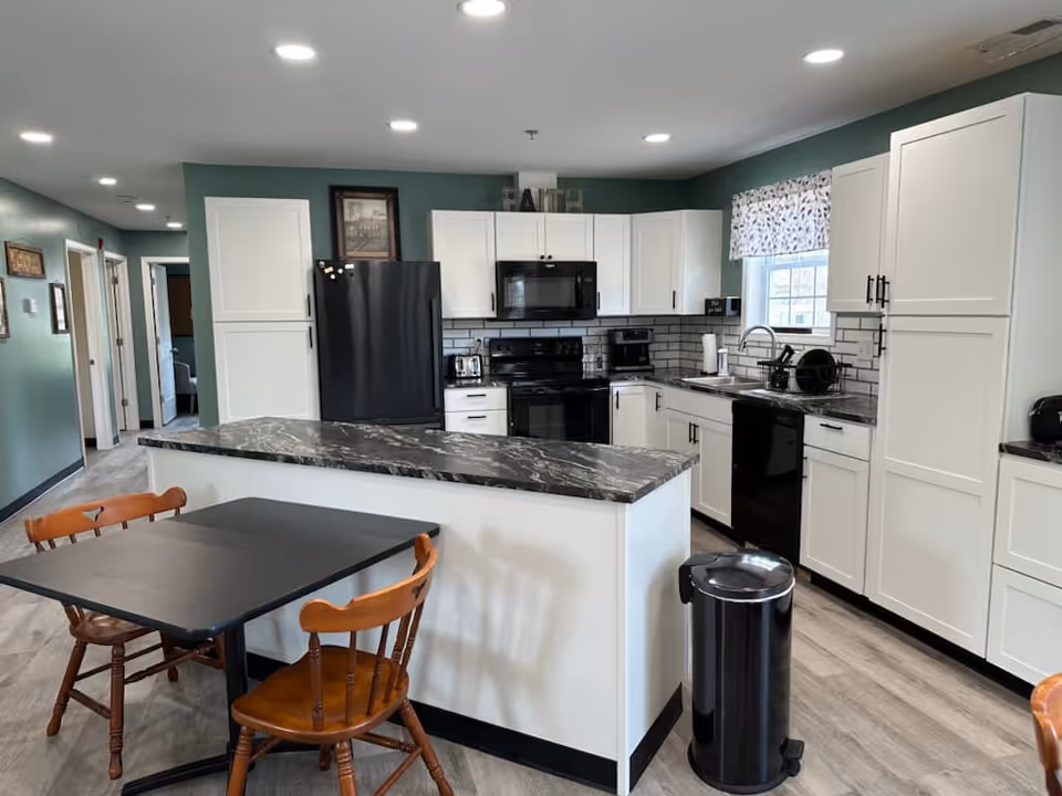 Bright kitchen with white cabinets, marble countertop island, and wooden dining table.