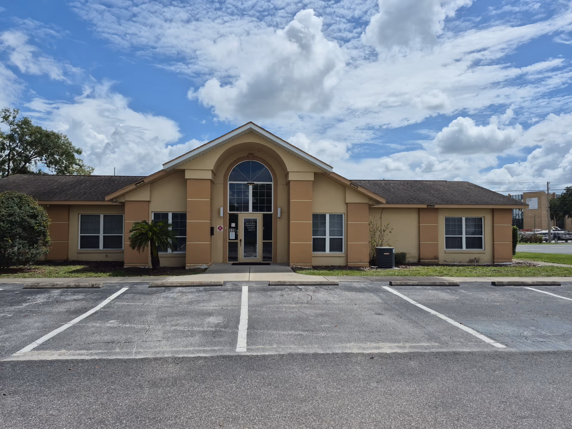 Front view of a single-story beige facility with arched entrance and a parking lot.