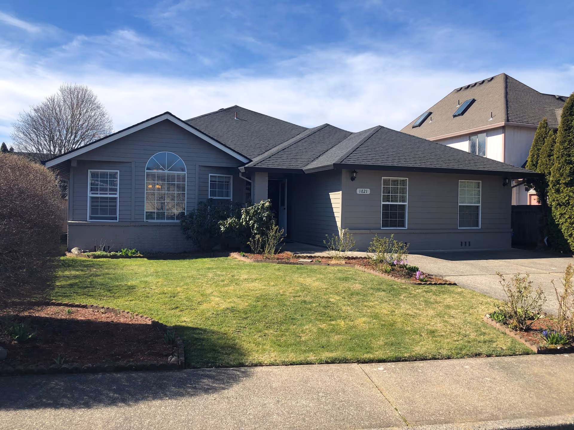 Front view of a single-story gray home with a manicured lawn and driveway