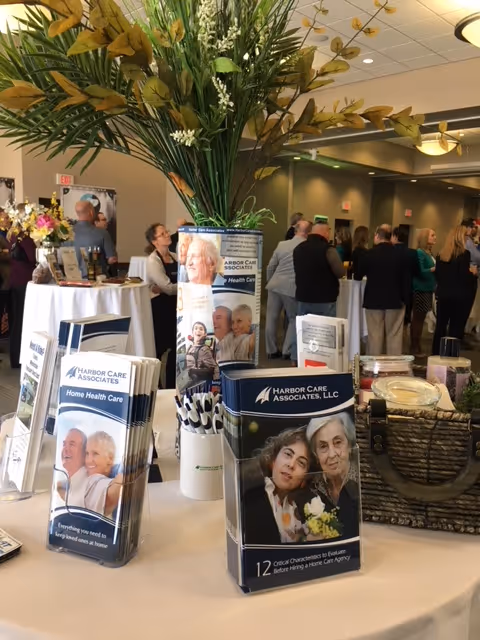 Indoor event with attendees browsing Harbor Care Associates brochures at a table with a floral centerpiece.