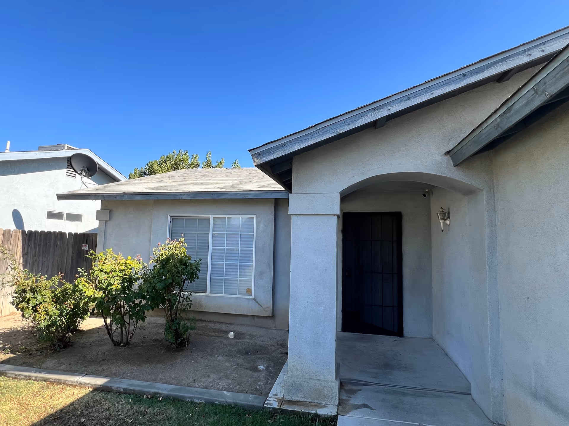 Single-story building exterior with a covered entry and small front yard shrubs.