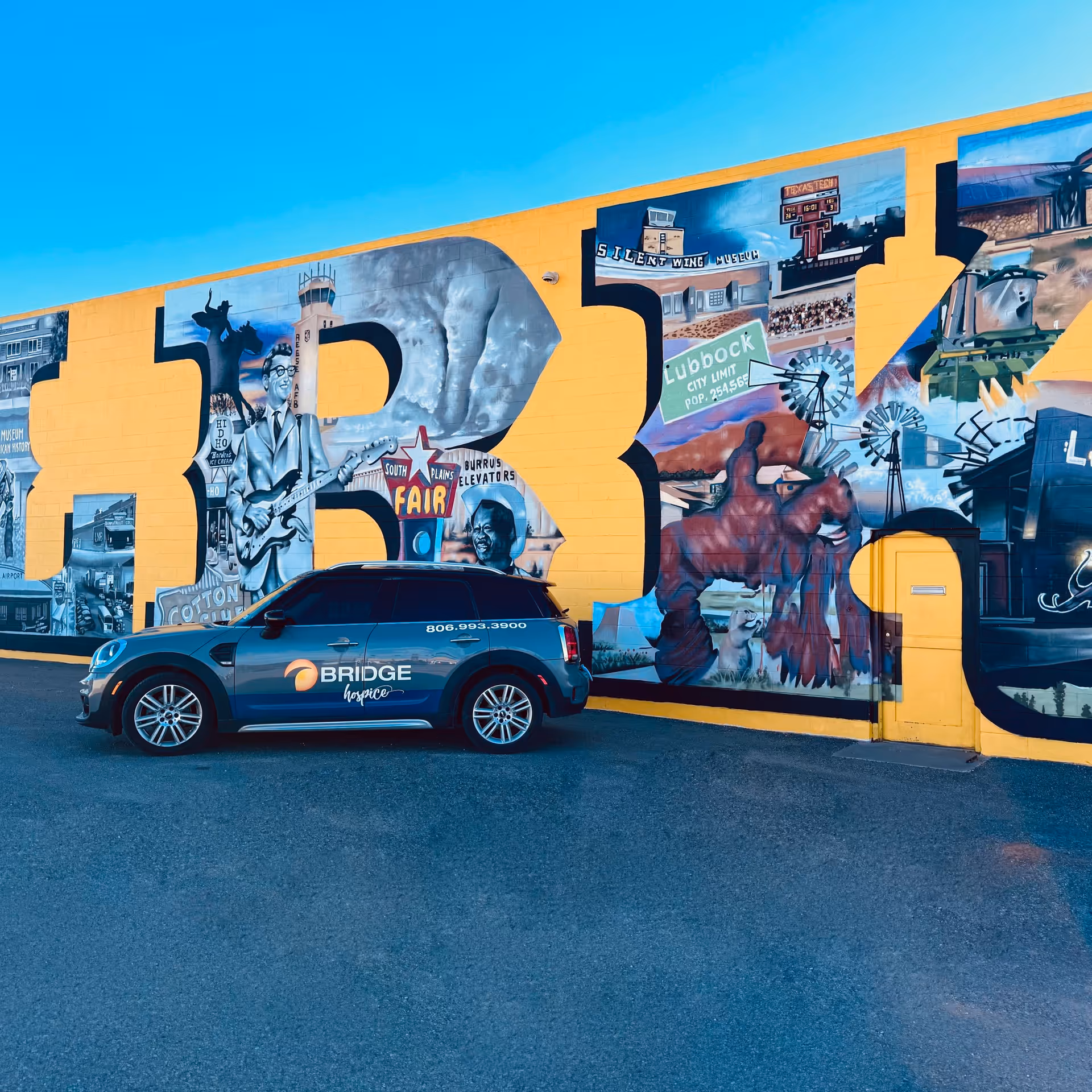 Blue BRIDGE Hospice van in front of a bright mural on a yellow building.