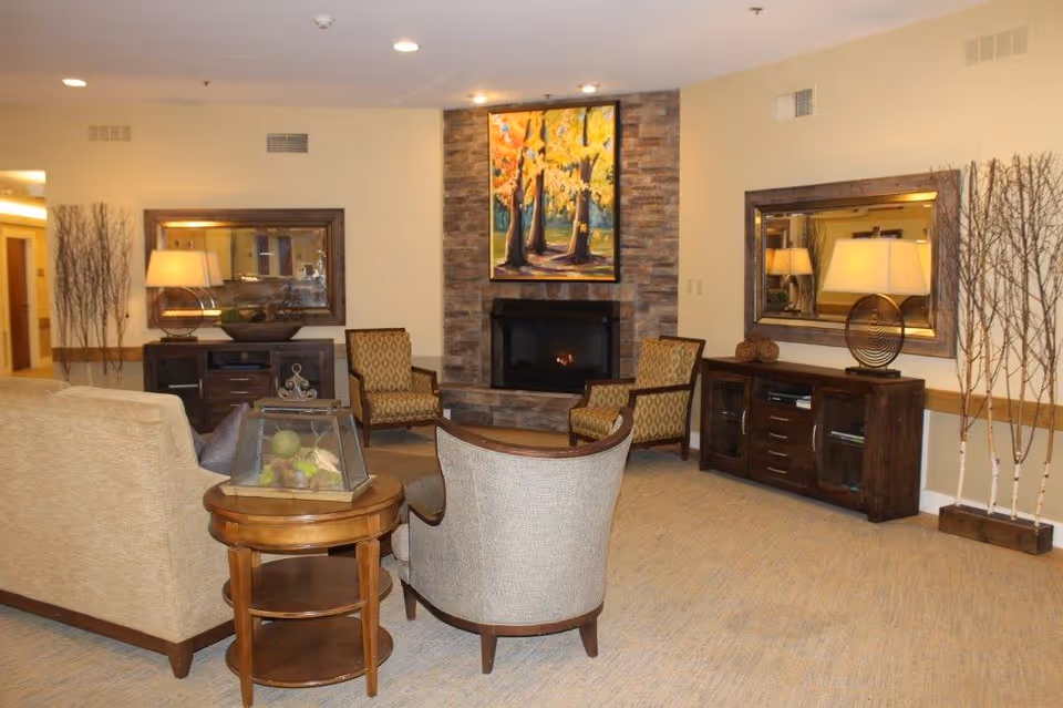 Cozy common living area with sofas and armchairs arranged around a stone fireplace topped with a painting.