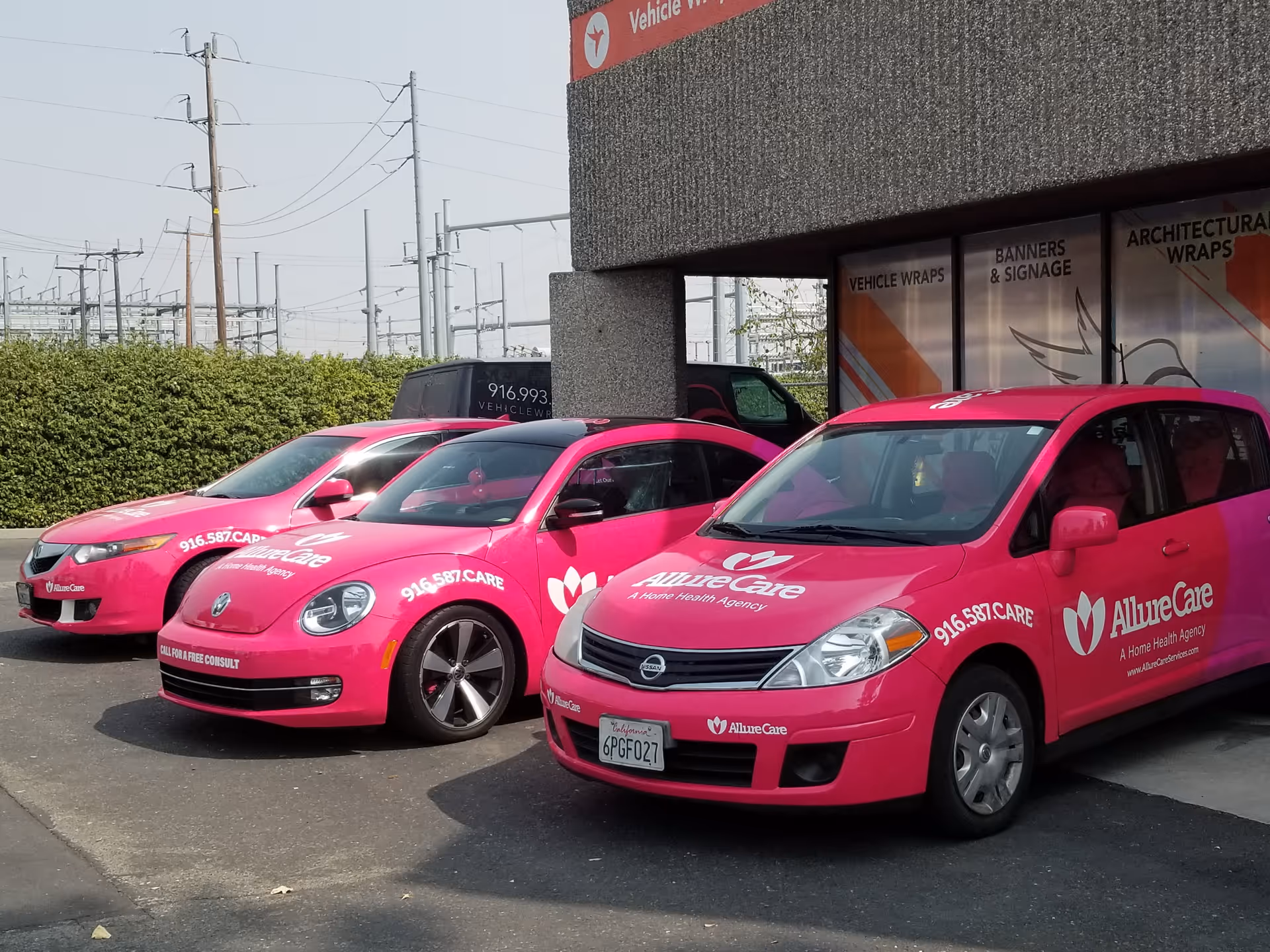 Three bright pink AllureCare vehicles parked outside a building with signage.