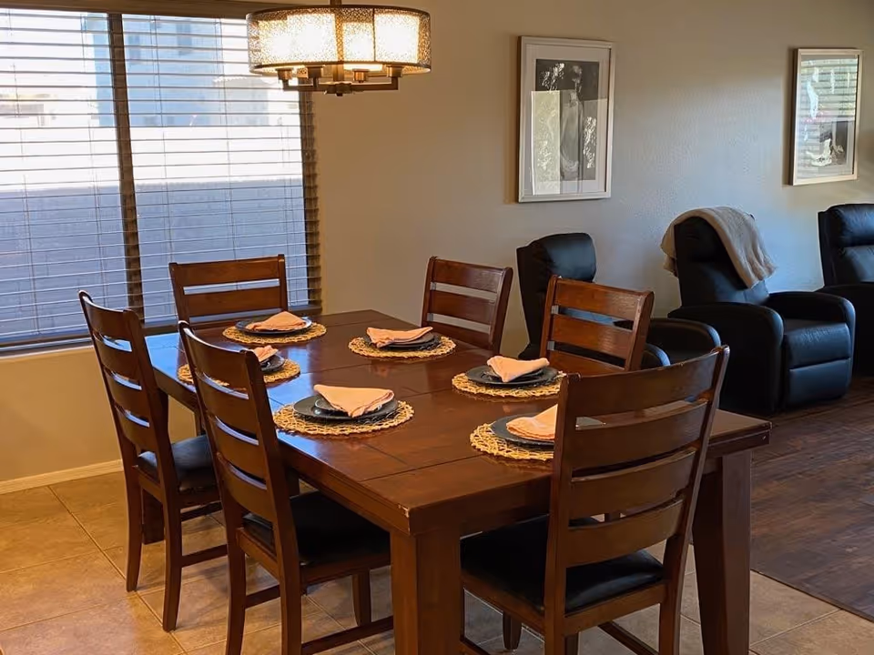 Wood dining table with six chairs and napkins in a bright dining area.