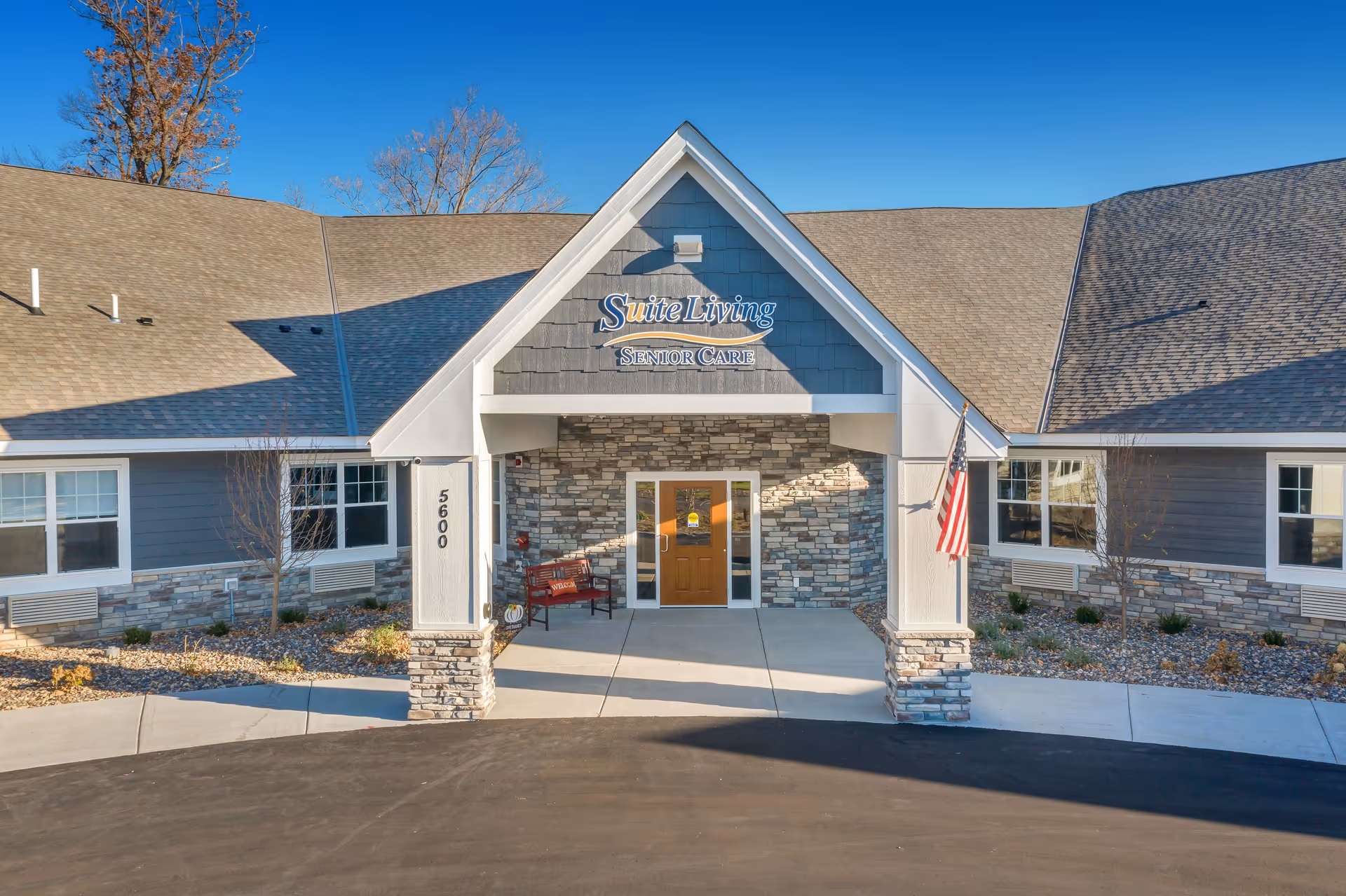 Front entrance of Suite Living Forest Lake, a single-story building with stone accents and American flag.