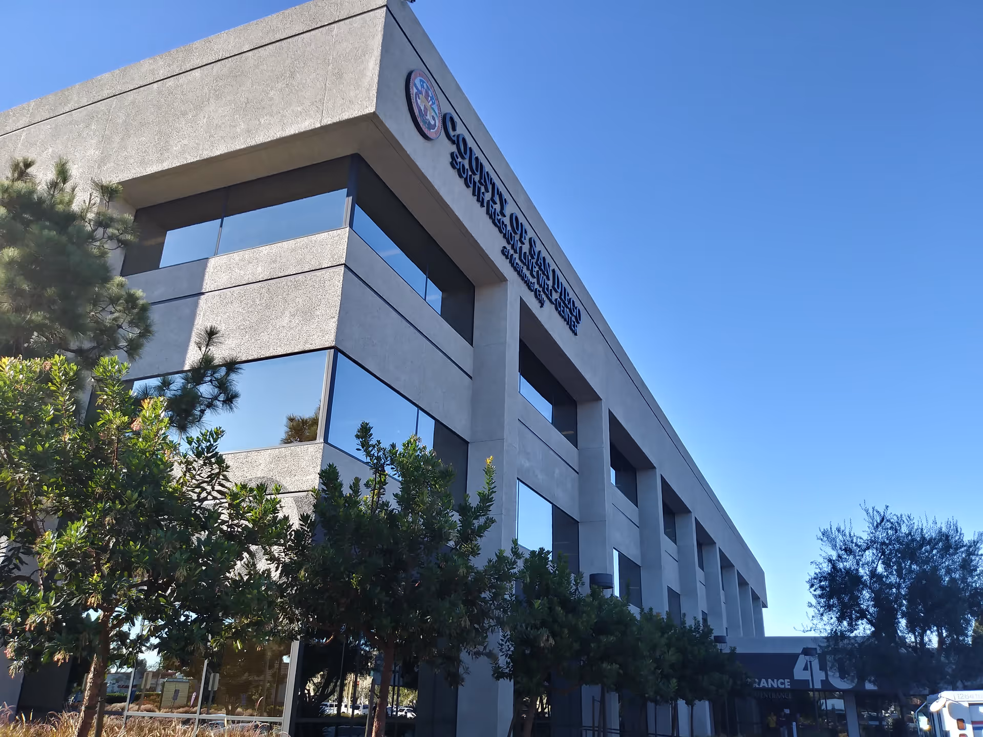 Exterior view of a modern building with trees, signage reading San Diego IHSS Public Authority.