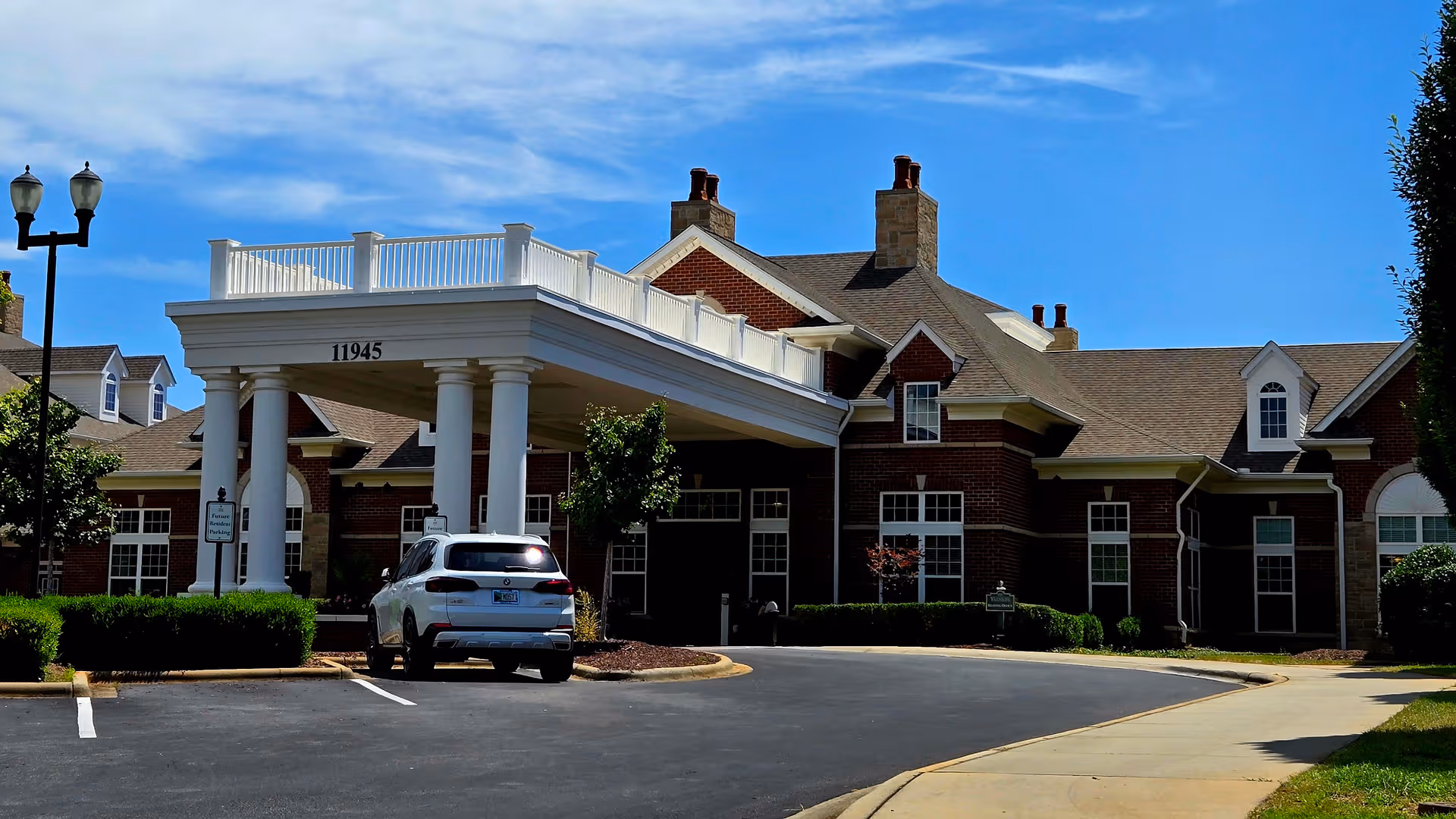 Exterior view of Waltonwood Providence entrance with a white porte cochere and a parked car.