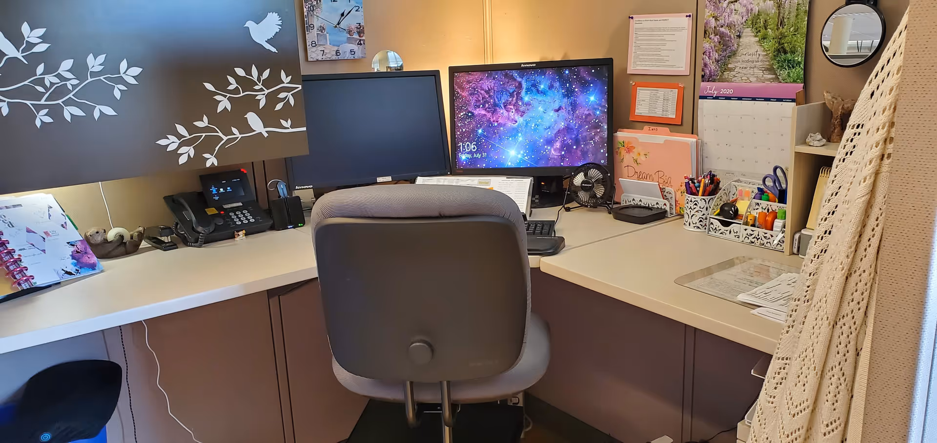 Office desk with two computer monitors, calendar, and office supplies inside a senior living facility.