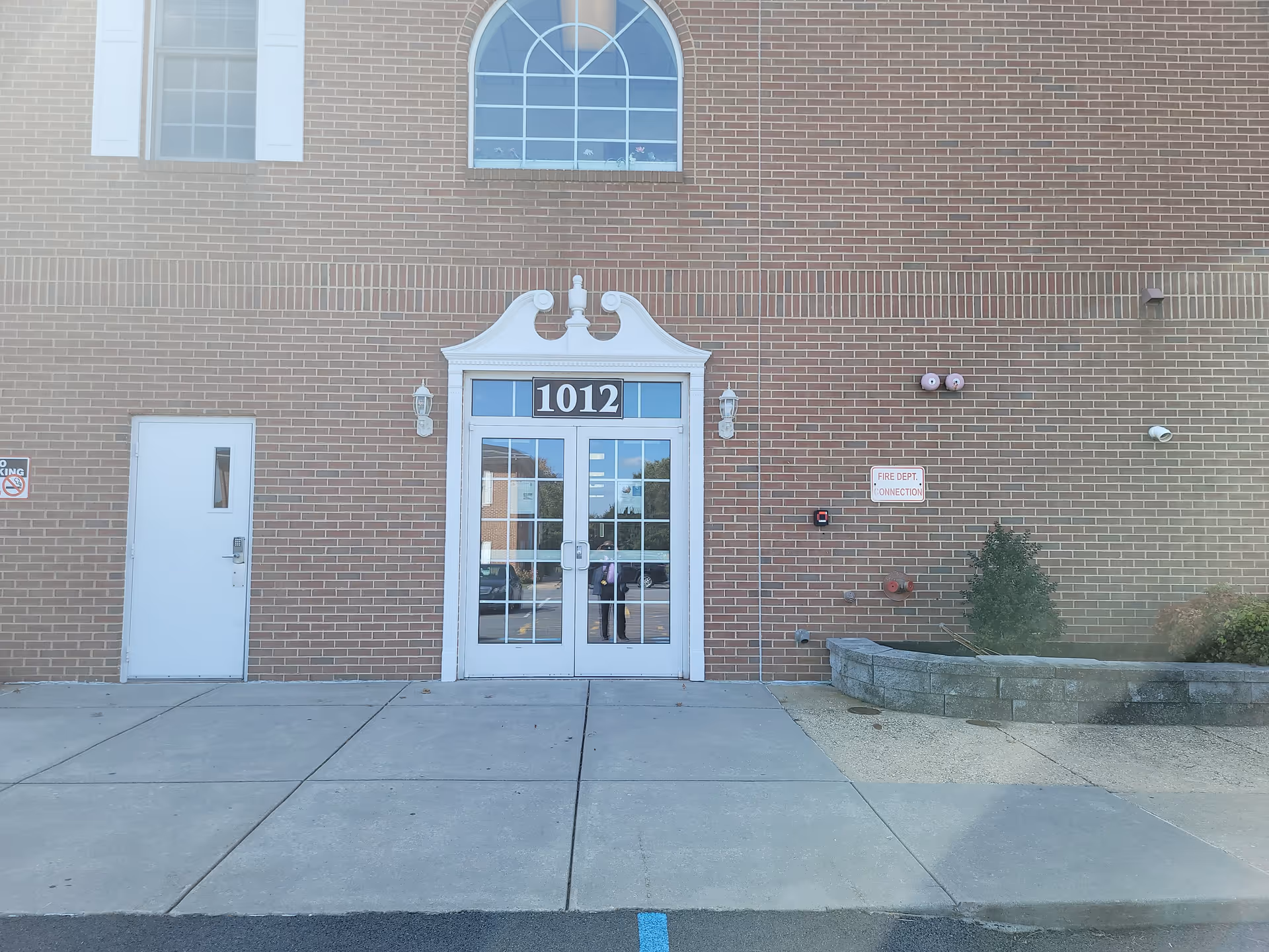 Brick building exterior with a decorative white entryway and glass doors labeled 1012.