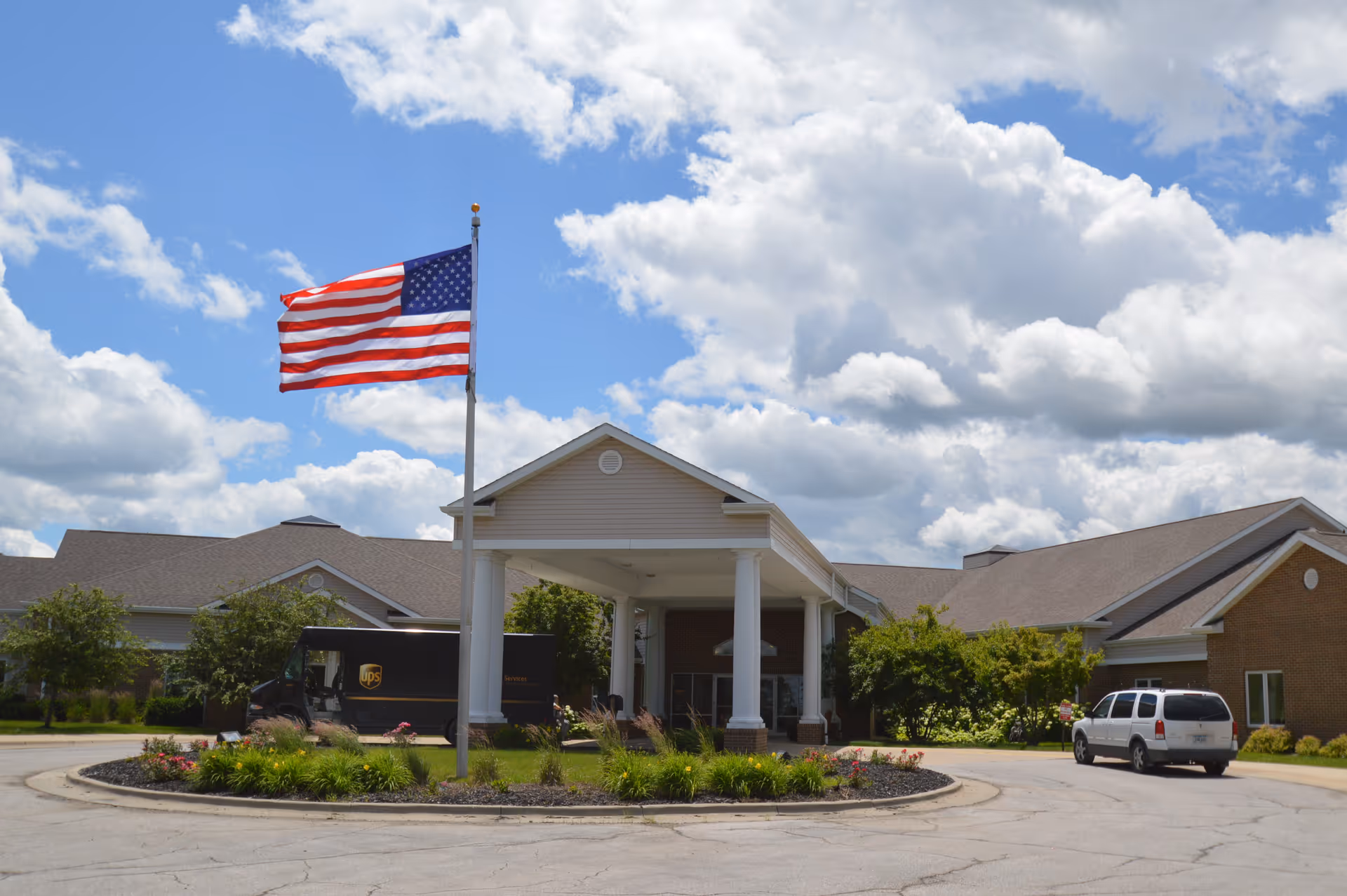 Front exterior view of Southern Hills Specialty Care building with a covered entrance, an American flag on a flagpole, a UPS delivery truck, and a white SUV parked nearby under a partly cloudy sky.