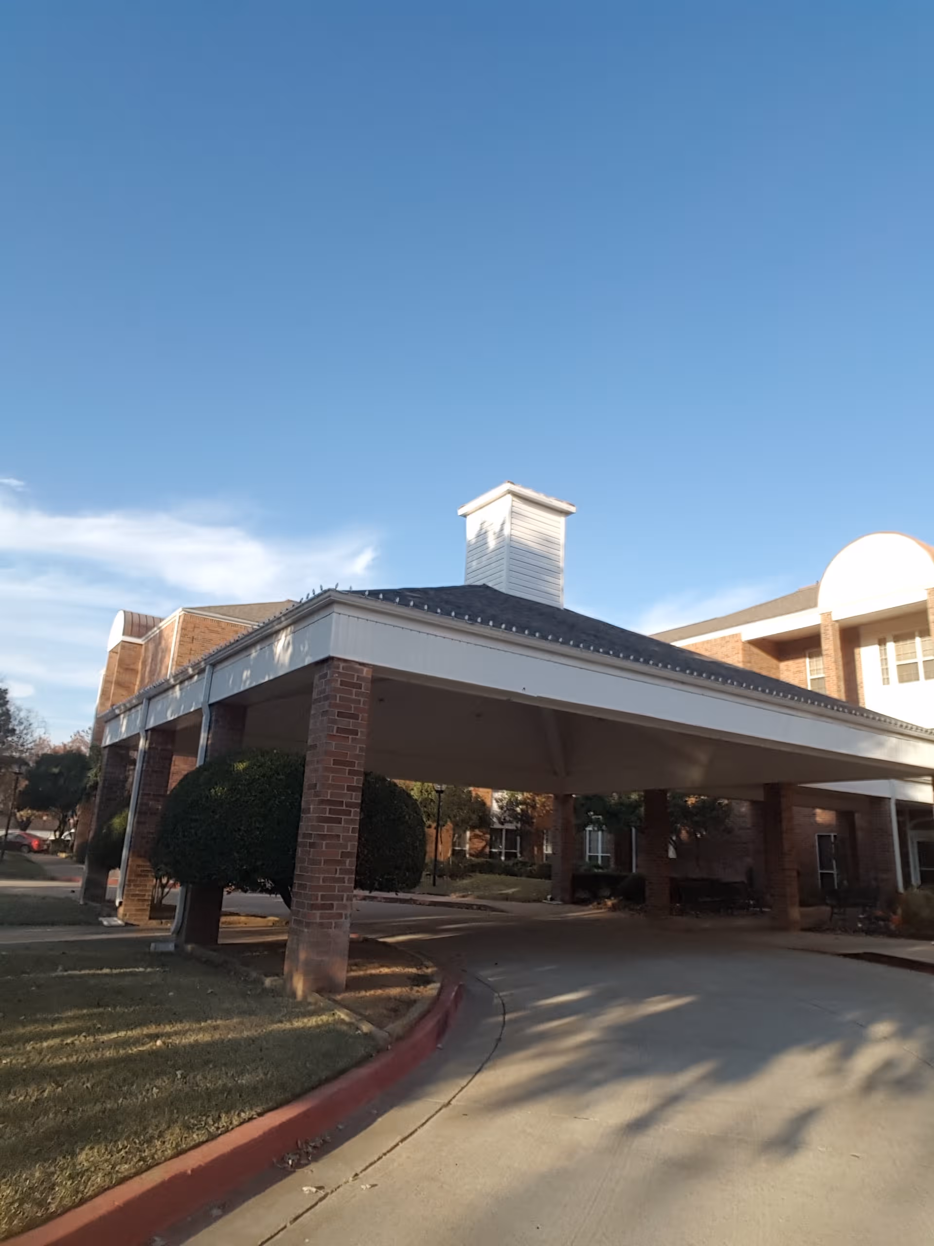 Rivermont Independent Living facility entrance with brick columns and a covered driveway under blue sky.