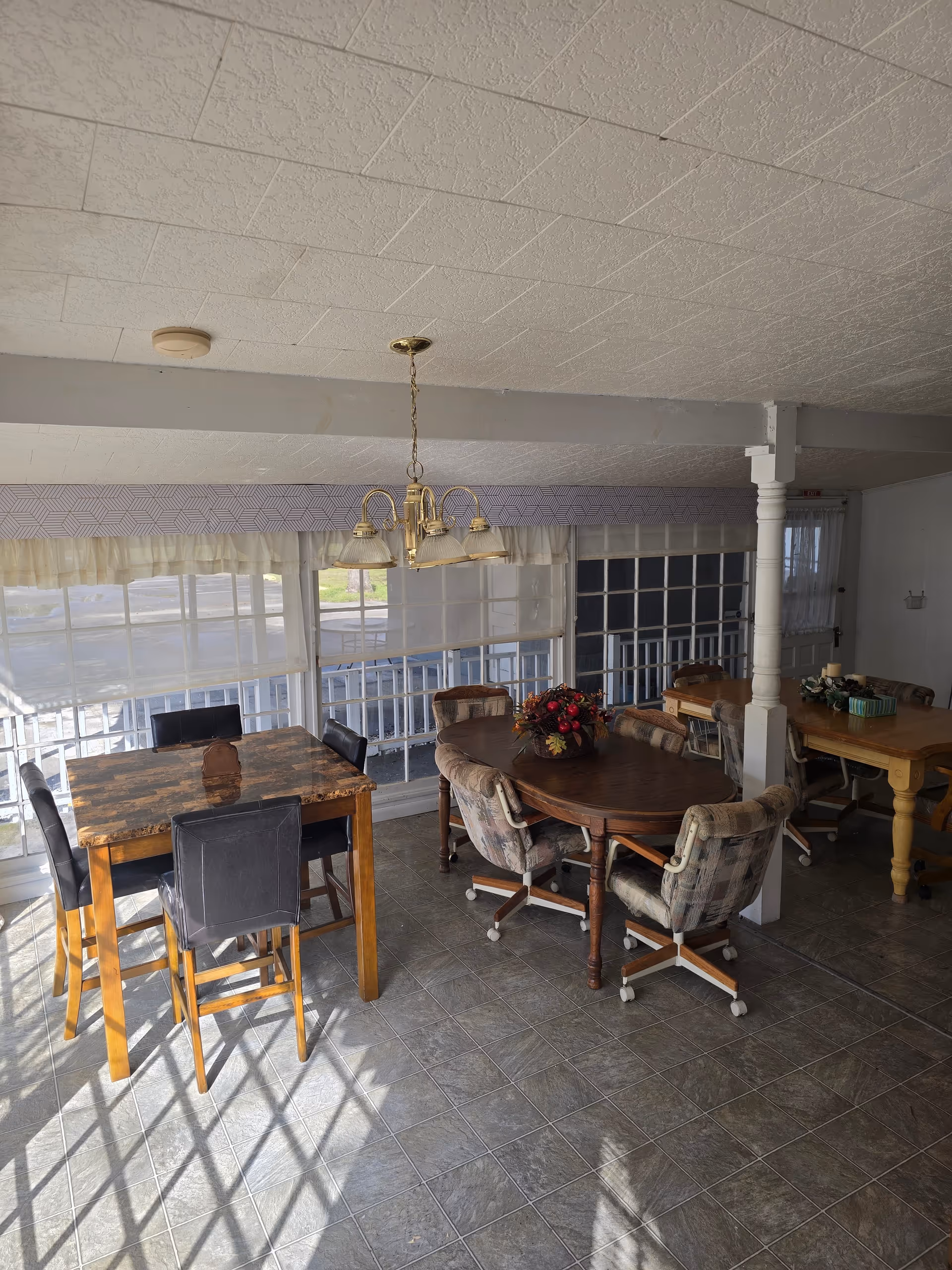 Indoor dining area with tables, chairs, and sunny windows at a senior care facility.