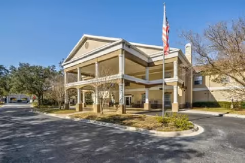 Front view of a senior living facility with a covered entrance and flagpole.
