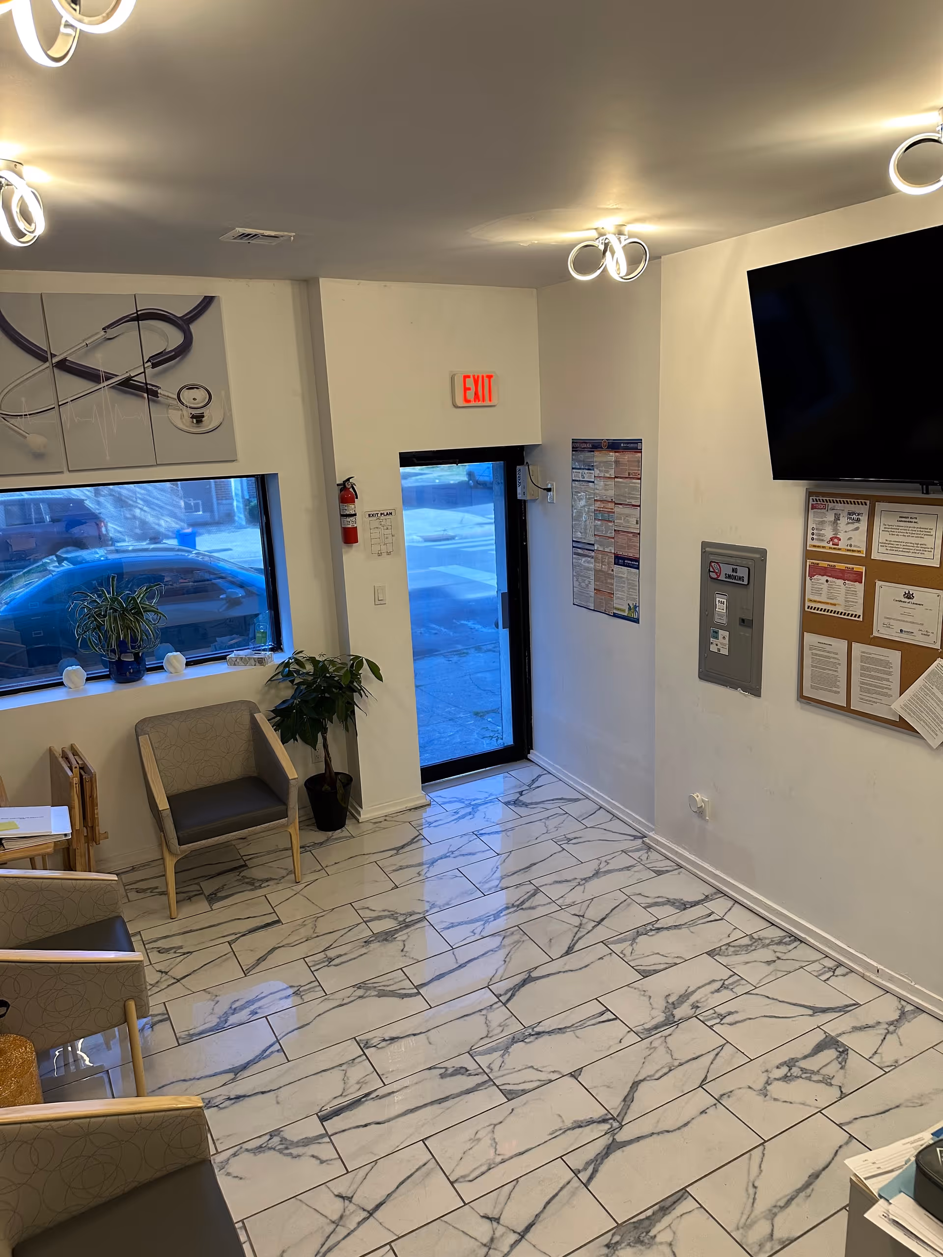 Bright interior lobby with marble tiles, seating, plants, bulletin board, and an exit door.