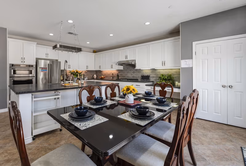 Bright modern kitchen with white cabinets and a black dining table set for six, featuring sunflowers.