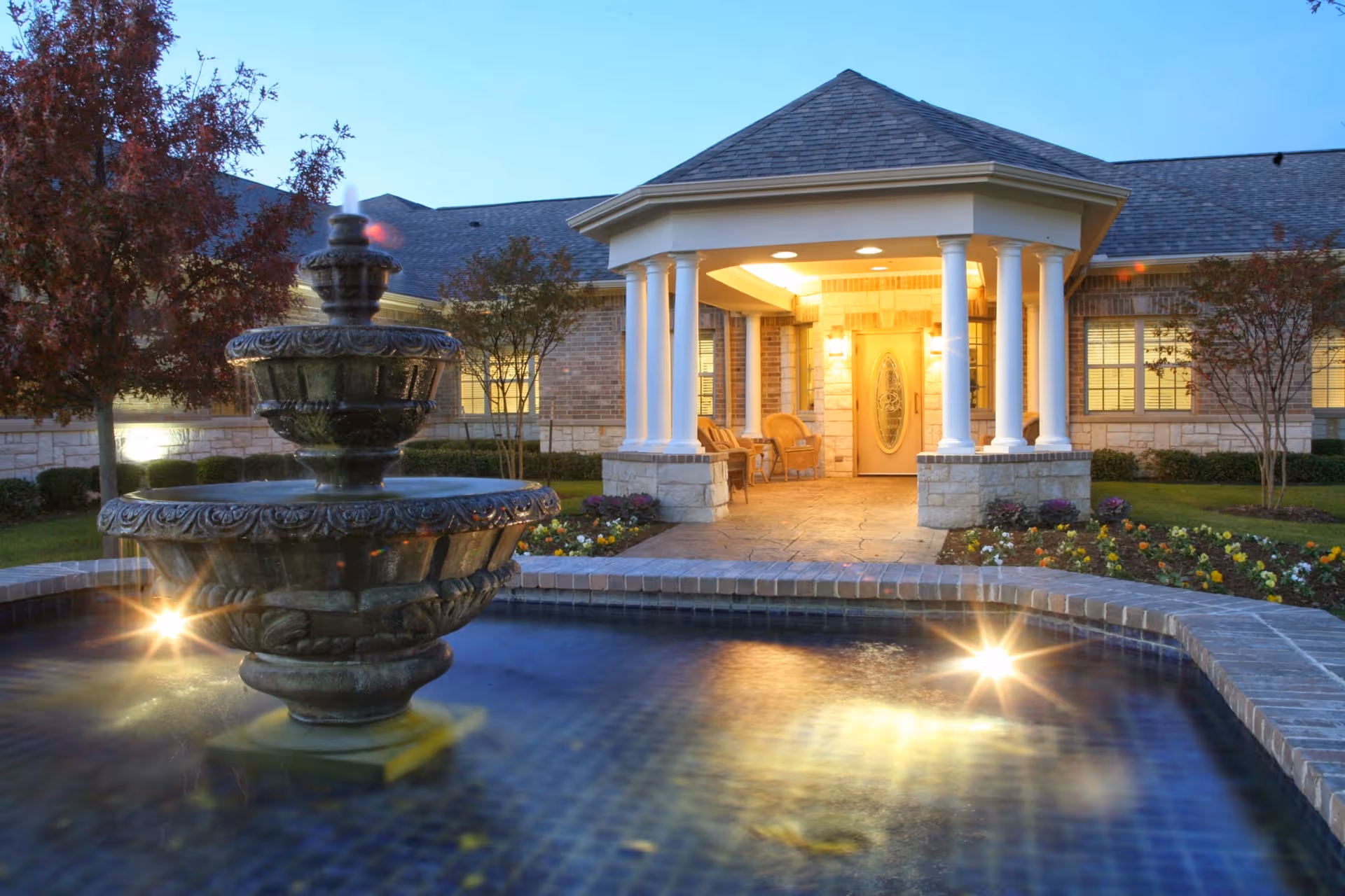 Front entrance of Grand Brook Memory Care of McKinney with a lit porch and fountain.